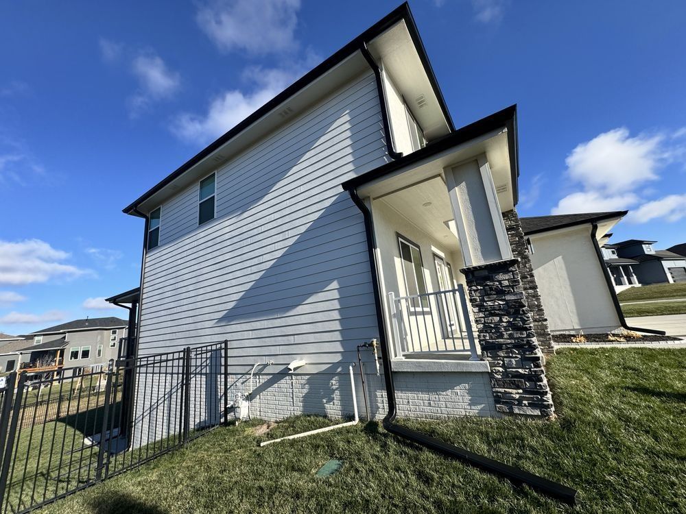 Modern two-story house exterior with white siding, black trim, front porch, and small fenced yard