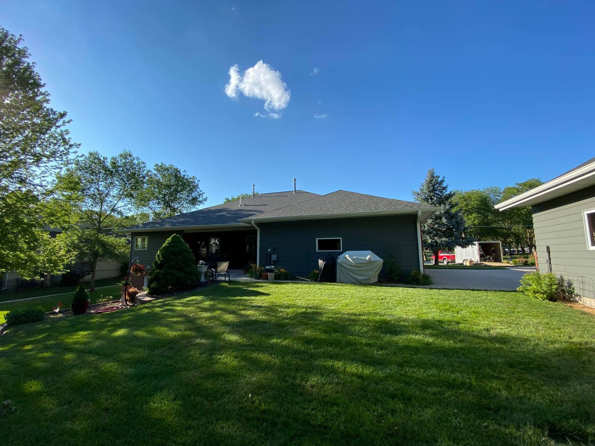 Backyard with green lawn, blue sky, and a house with patio and shed.