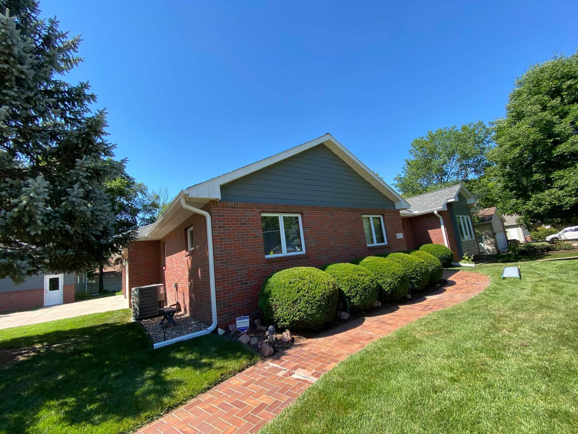 Brick house with green lawn, red brick walkway, and trimmed bushes under a blue sky