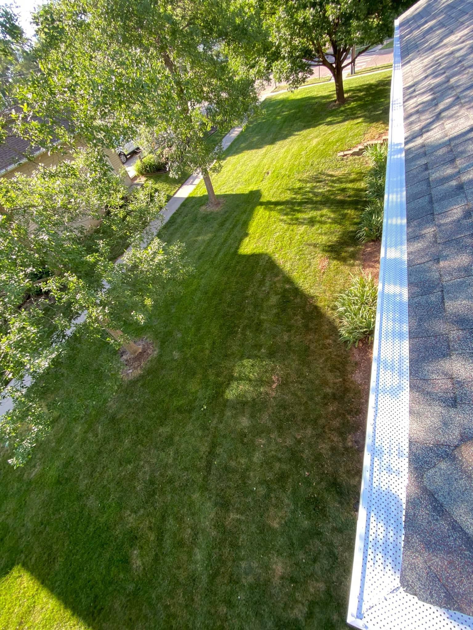 Sunlit grassy backyard beside a white house, with trees and a sloped lawn.