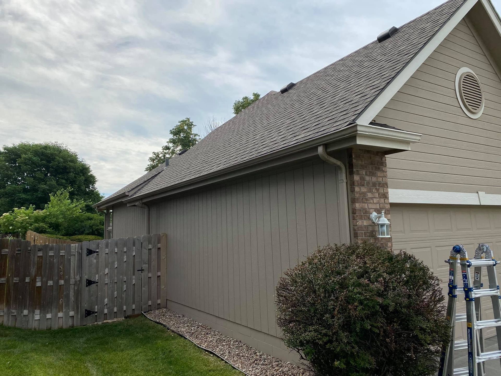 Gray house exterior with fenced side yard, shrubs, and utility meters near the wall
