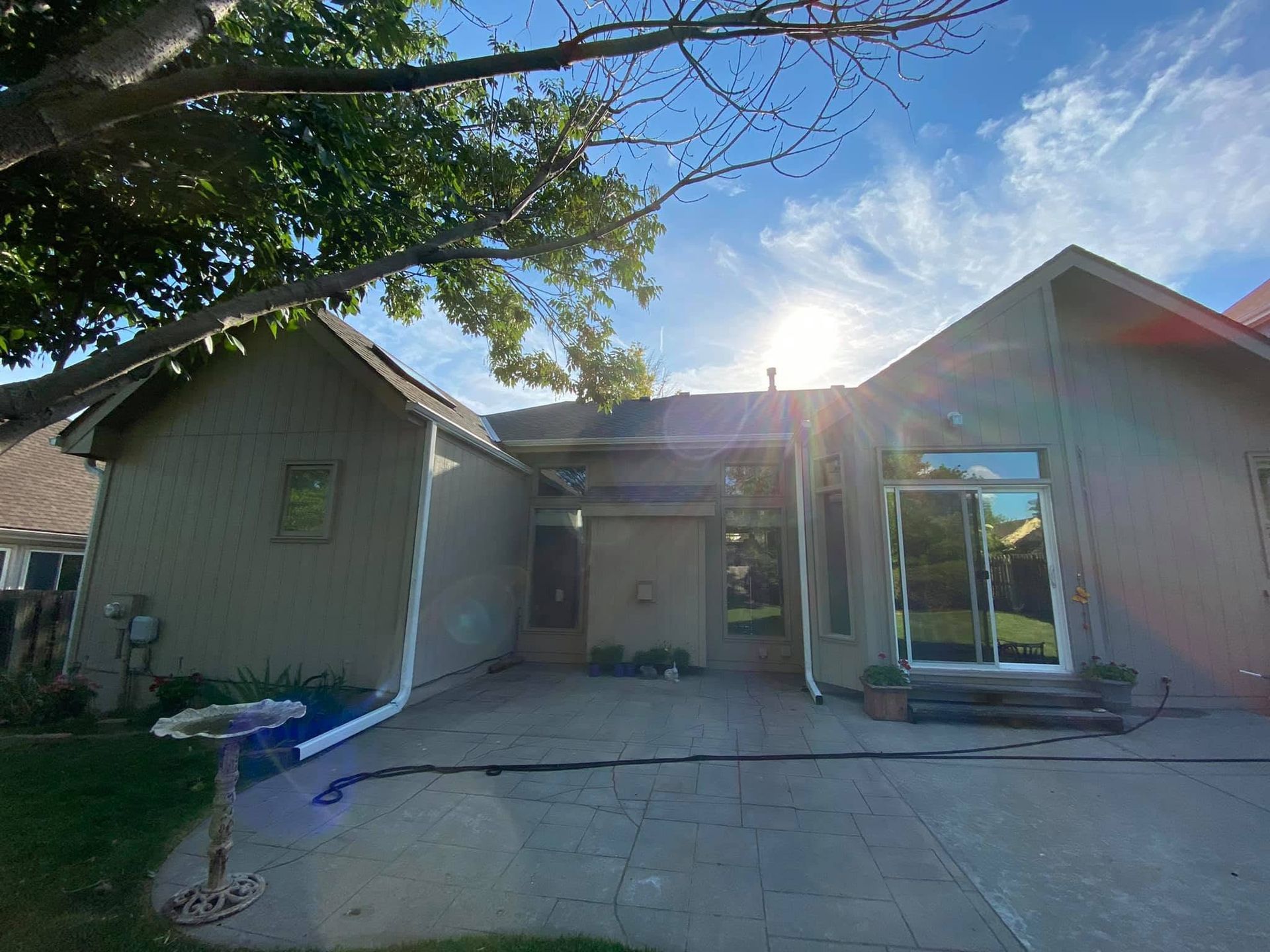 Single-story house exterior with a front driveway, garage, and bright sunlight behind the roofline.