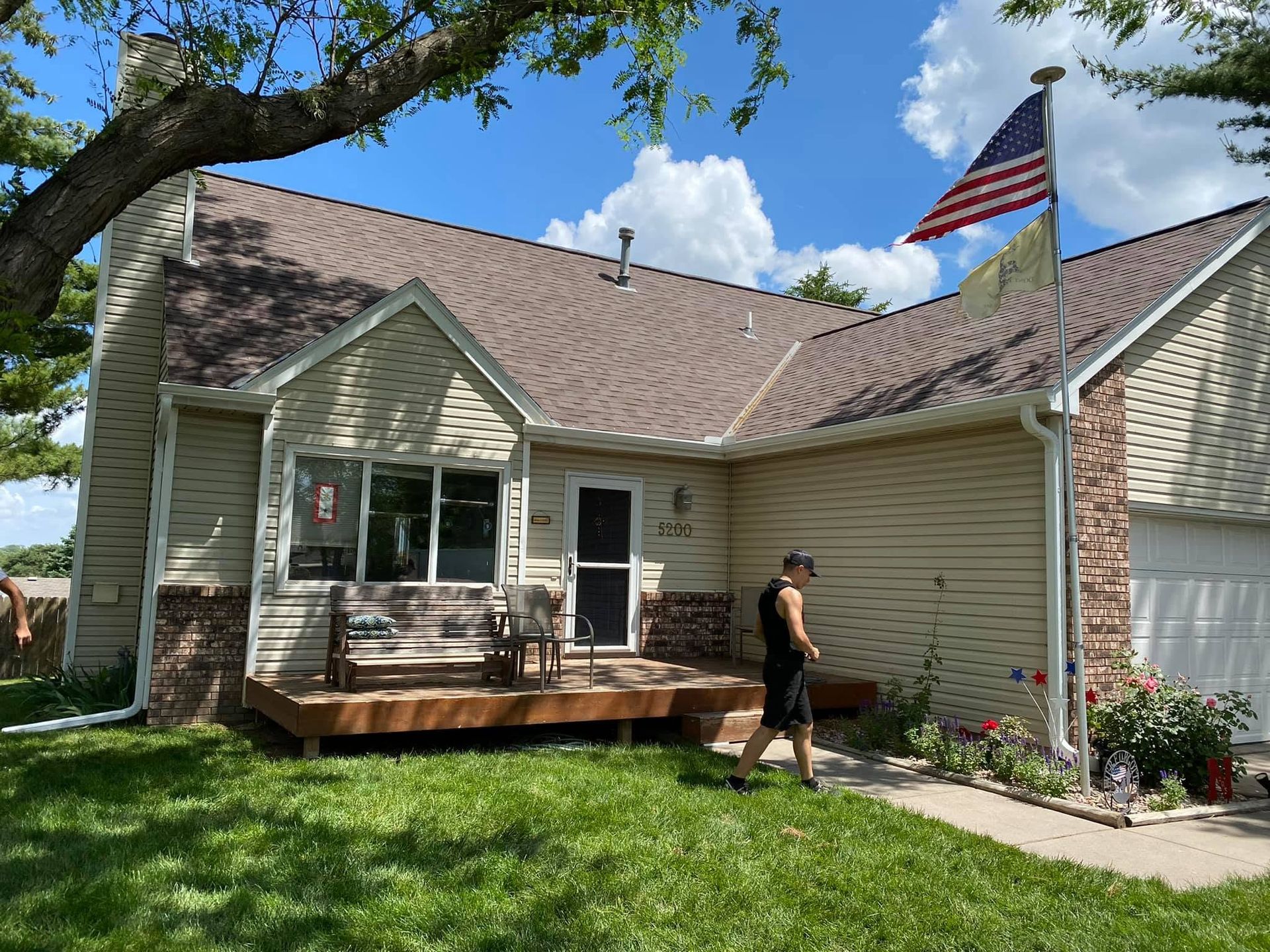 Small beige house with a porch, American flag, and person walking on the sidewalk in front.