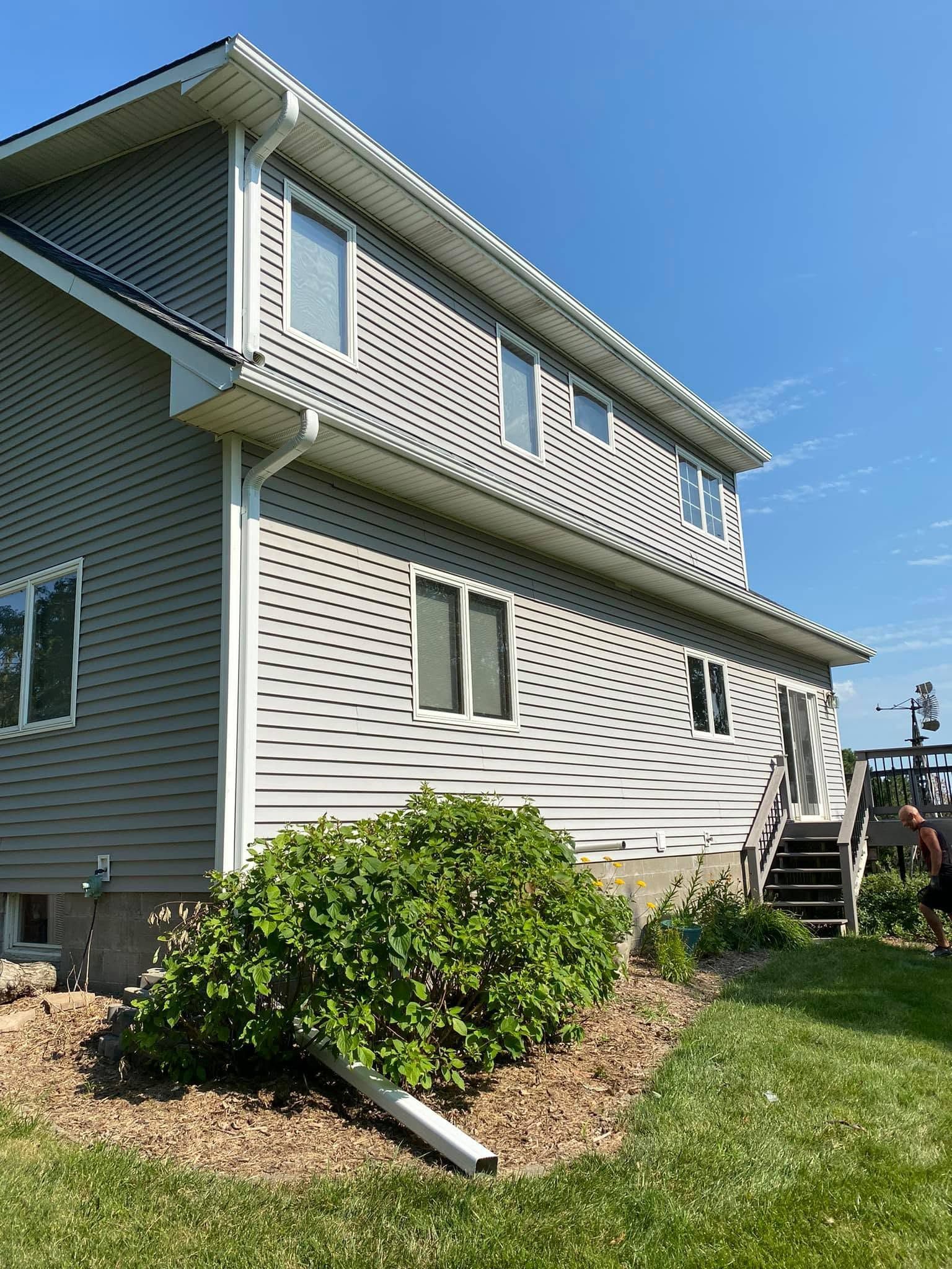 Two-story light gray house with white lattice siding, blue sky, and a small front yard shrub.