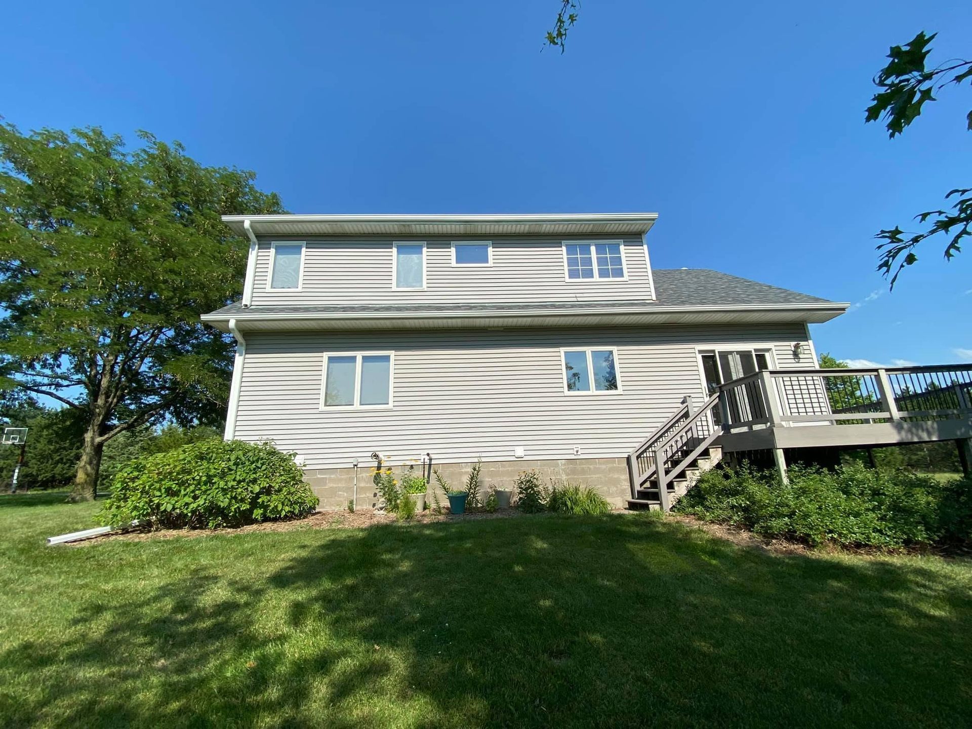 White two-story house with a front deck, stairs, and green lawn under a blue sky