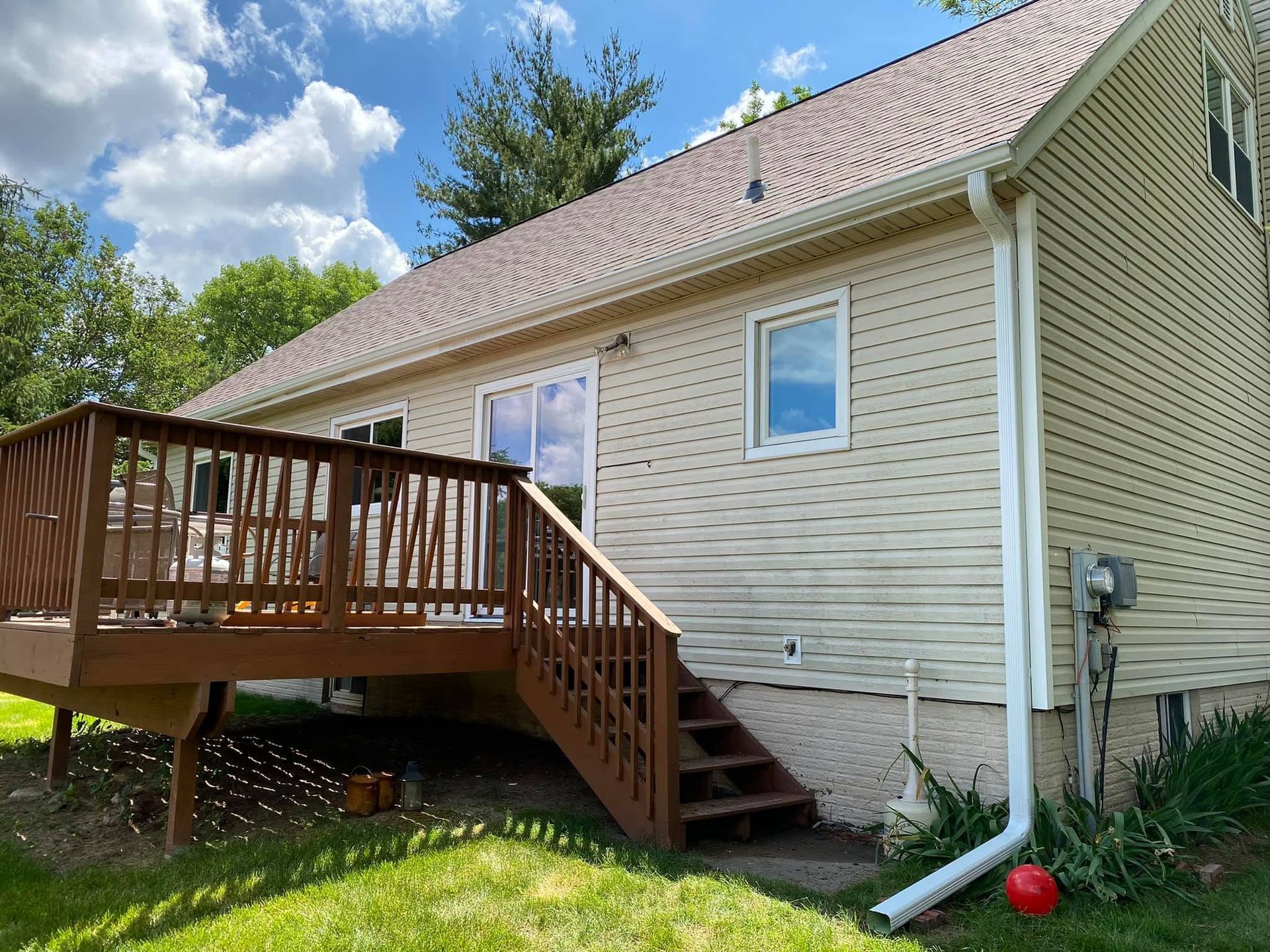 Back porch deck with stairs on a beige house under a blue sky.