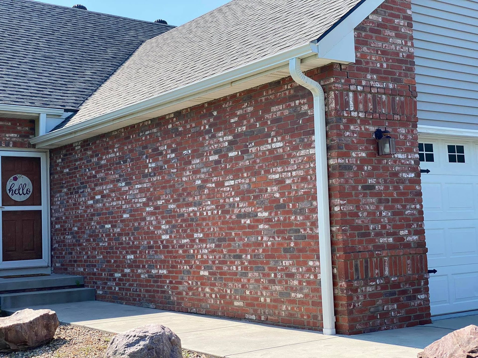 Brick house side wall with white gutter and downspout beside a garage door and front entry
