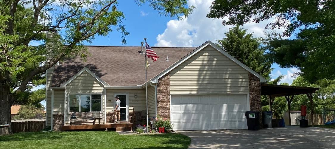 Small single-story house with a brick facade, beige garage, and front porch under a blue sky