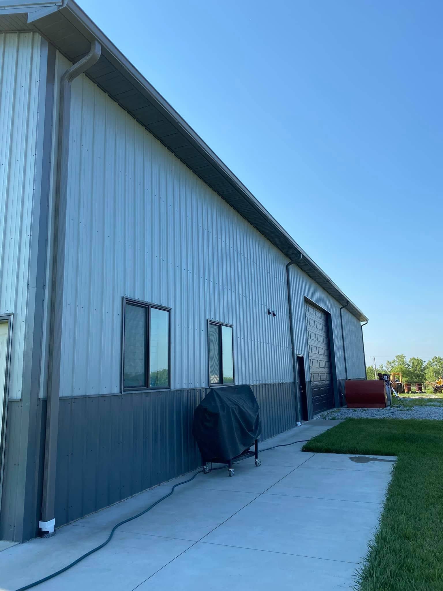 Metal-sided warehouse exterior with windows, a concrete walkway, and grass under a clear blue sky