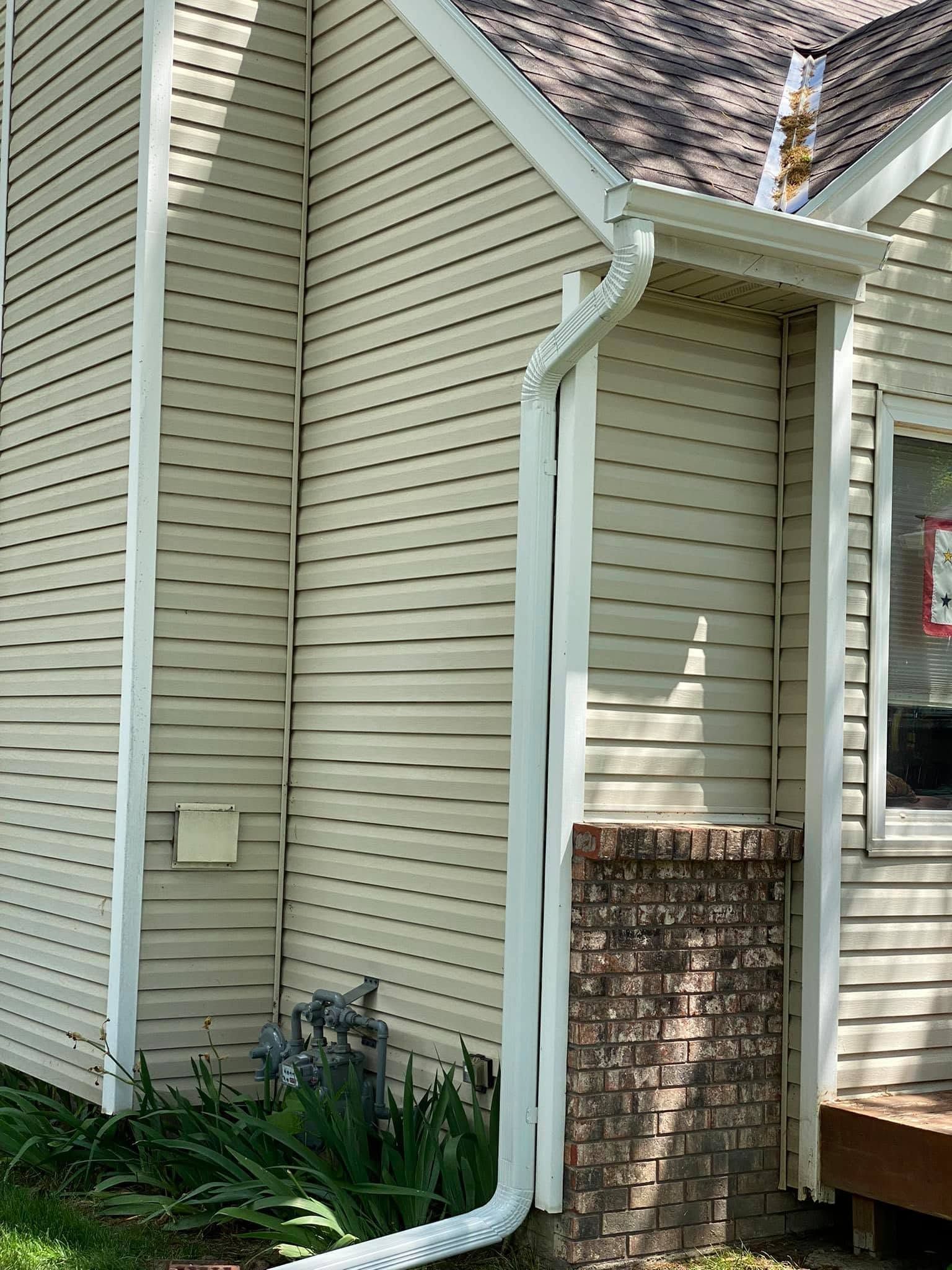 House exterior with beige siding, white downspouts, and a brick chimney beside a small deck