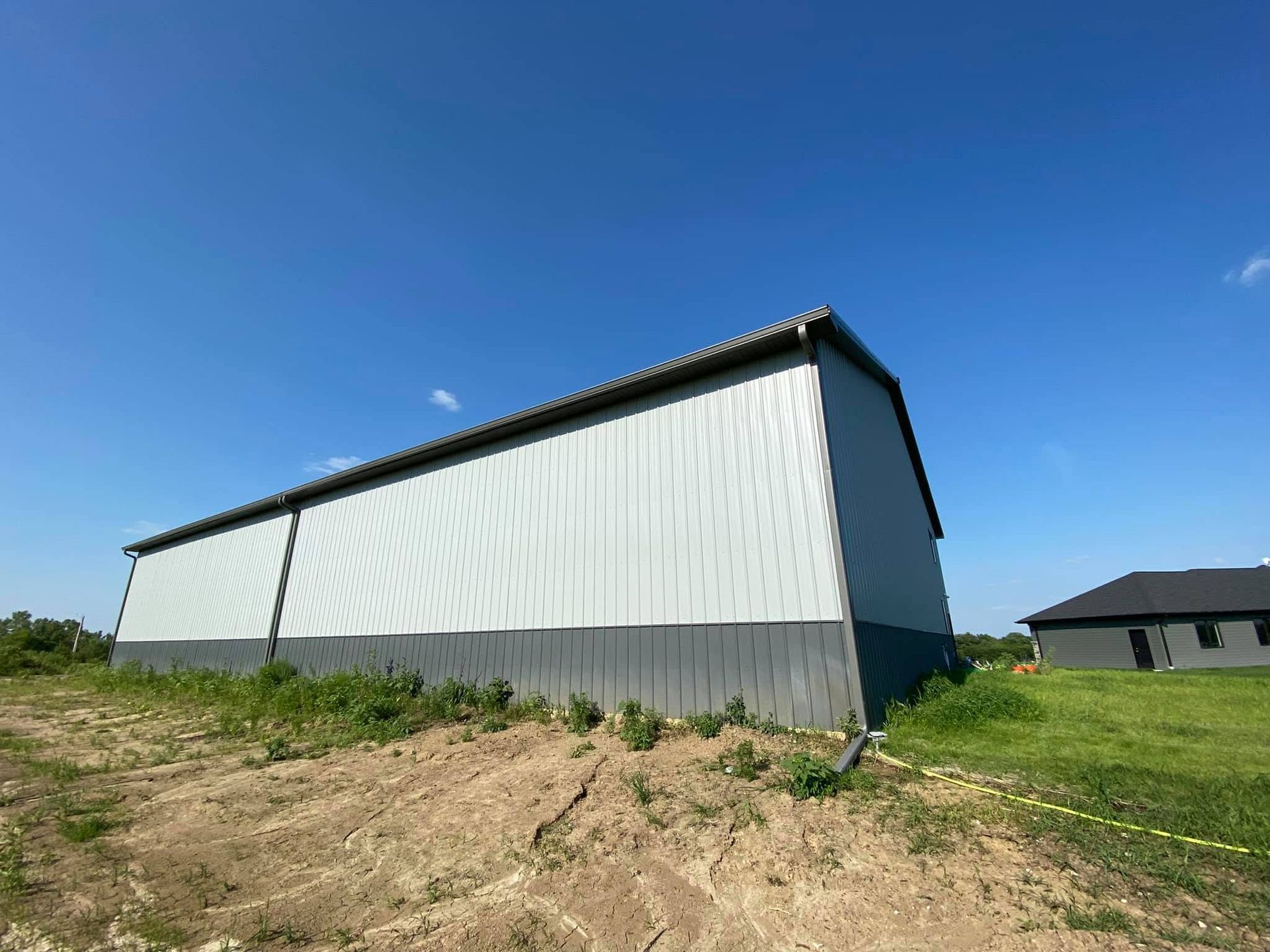 Long white barn with a dark roof on a dirt lot under a clear blue sky