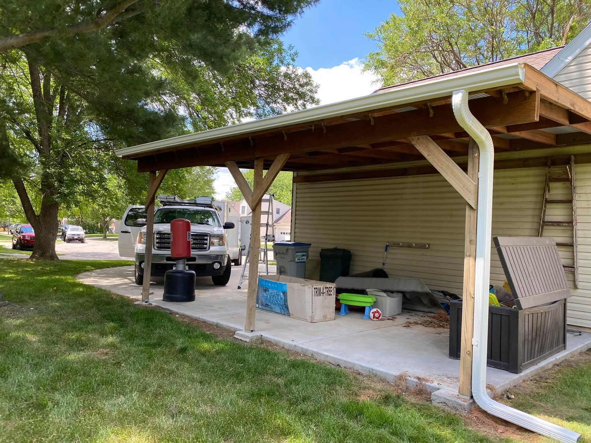 Backyard patio with covered porch, storage bins, grill, and a white pickup truck nearby