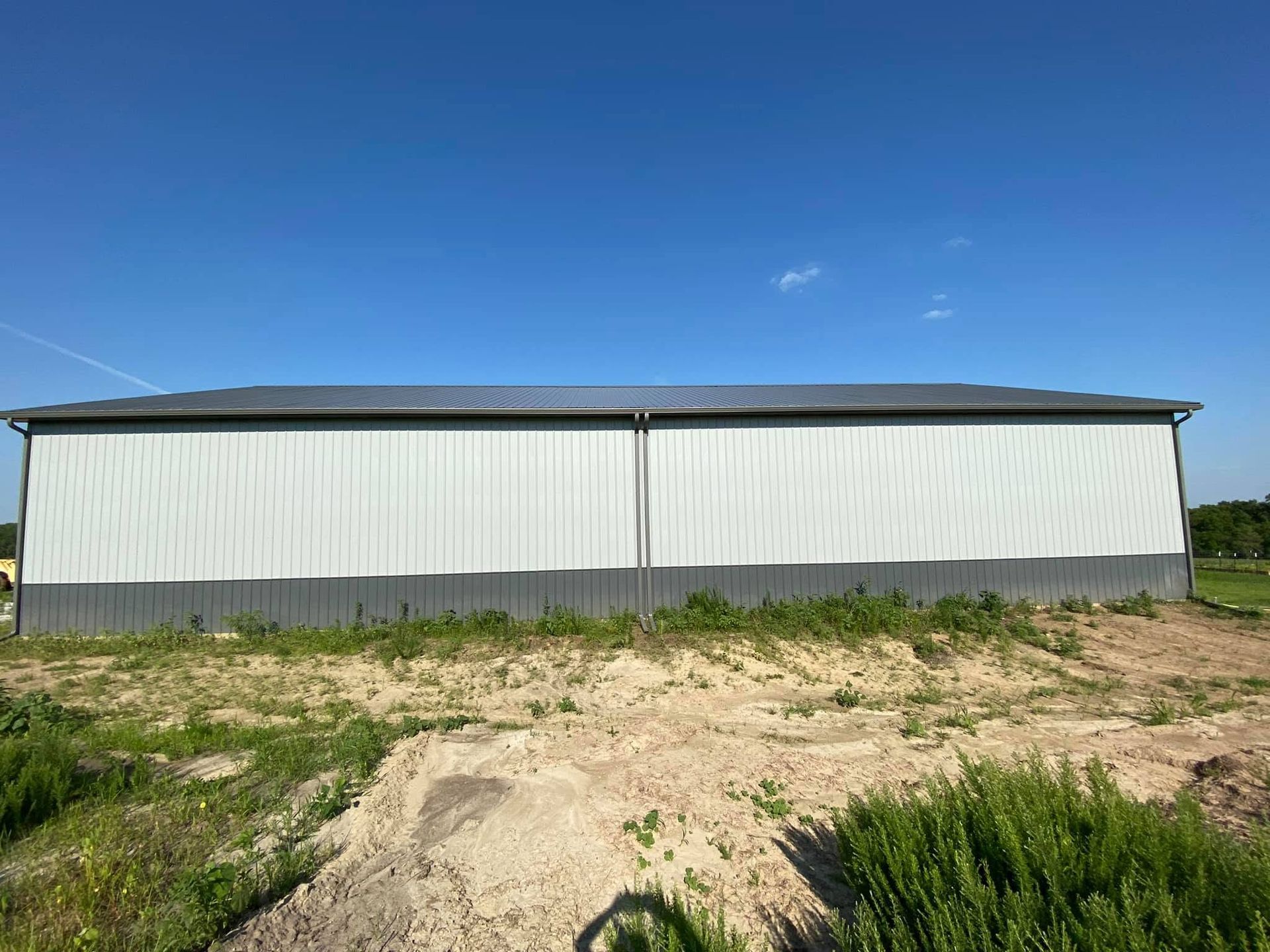 Long white metal barn under a blue sky, with a dirt foreground and grass around it