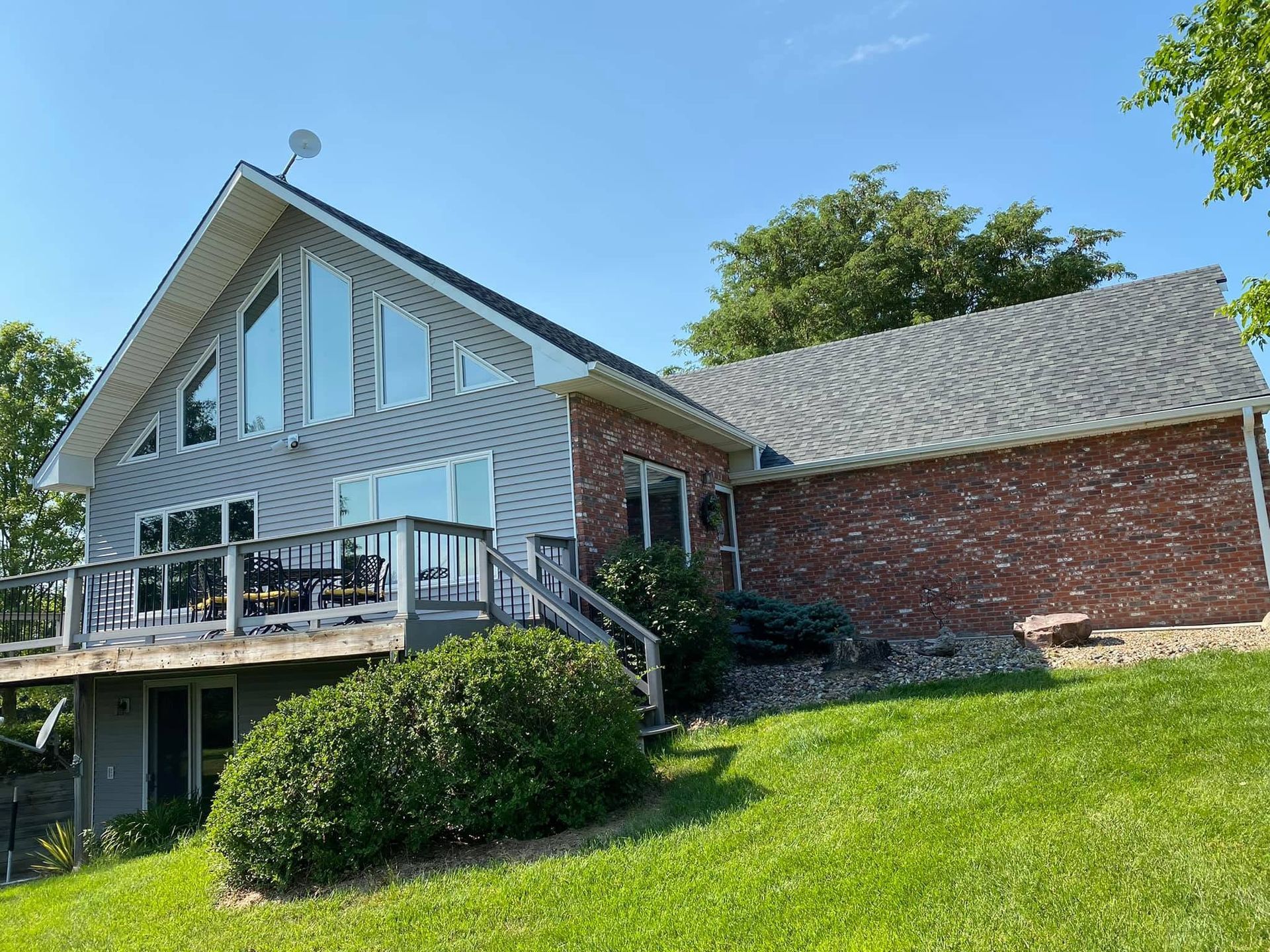 Brick house with a deck, large windows, and sloped roof on a grassy hillside under a blue sky