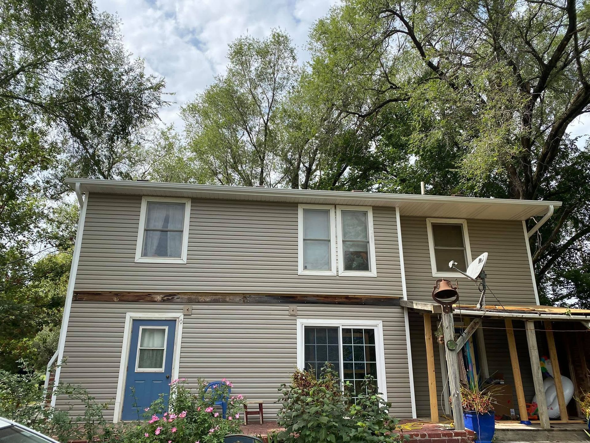 Two-story beige house with blue door and porch, surrounded by trees