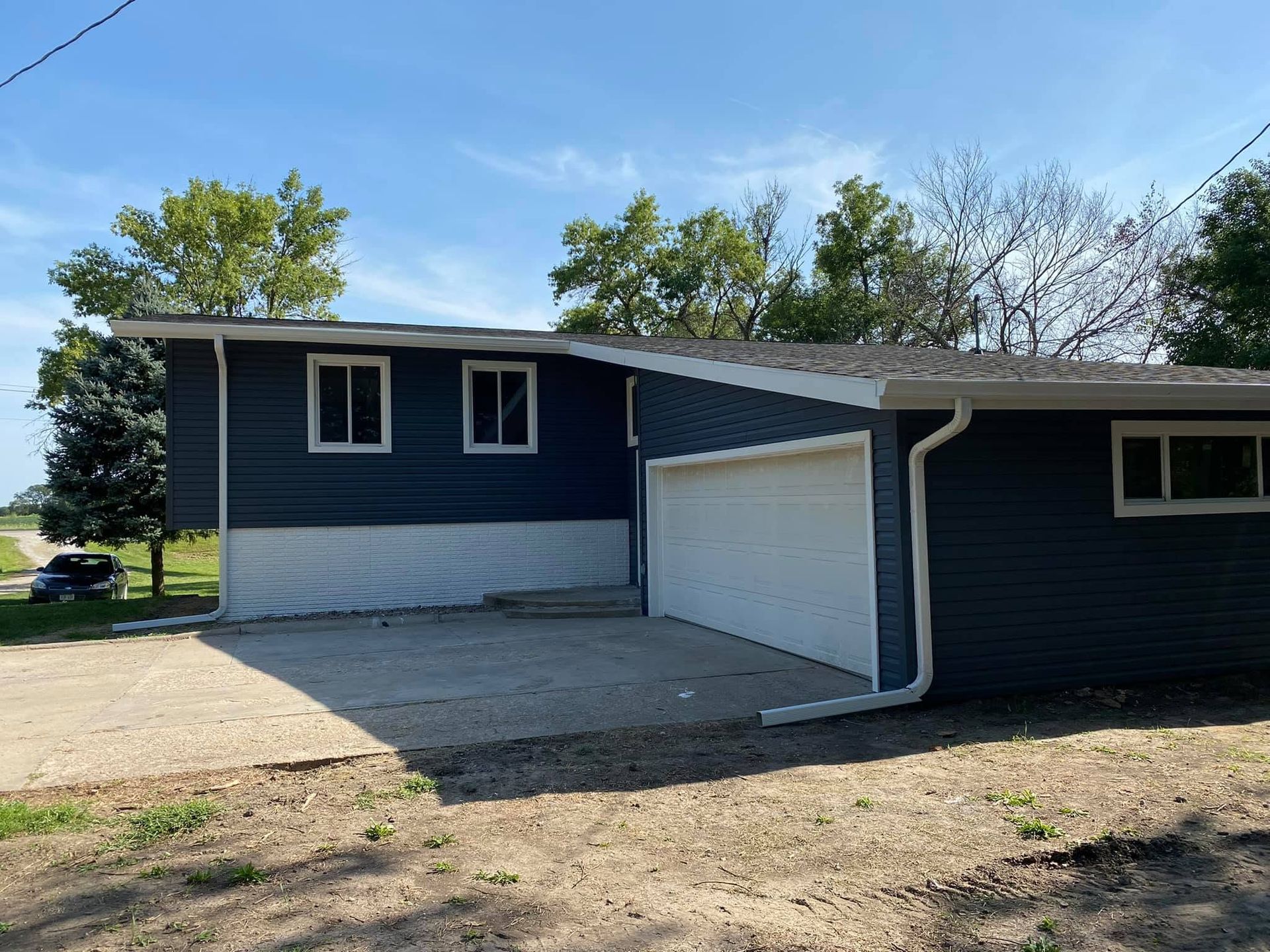 Blue and white house exterior with a garage, driveway, and trees under a clear sky