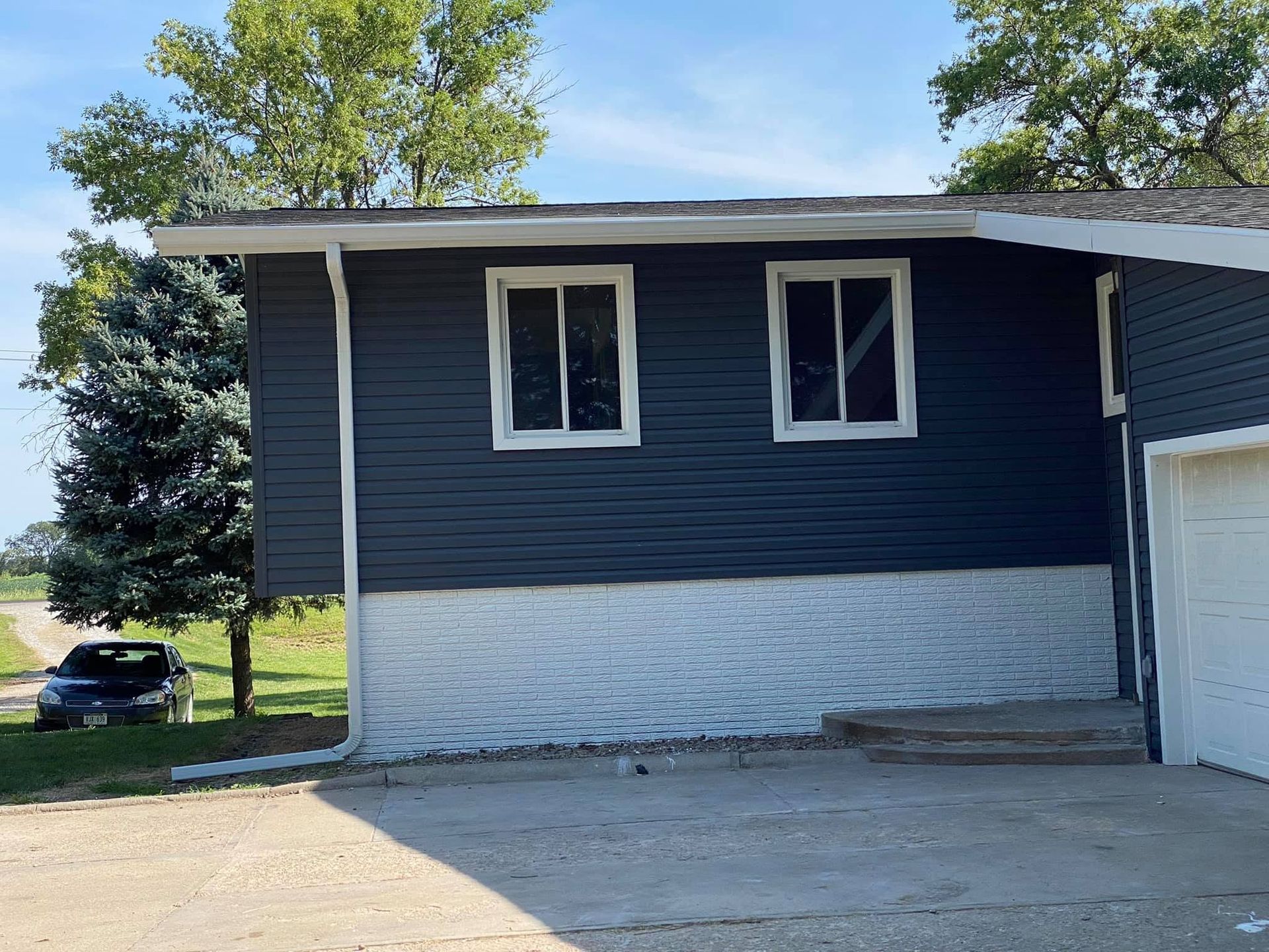 Blue house exterior with two windows, white trim, and a driveway in front