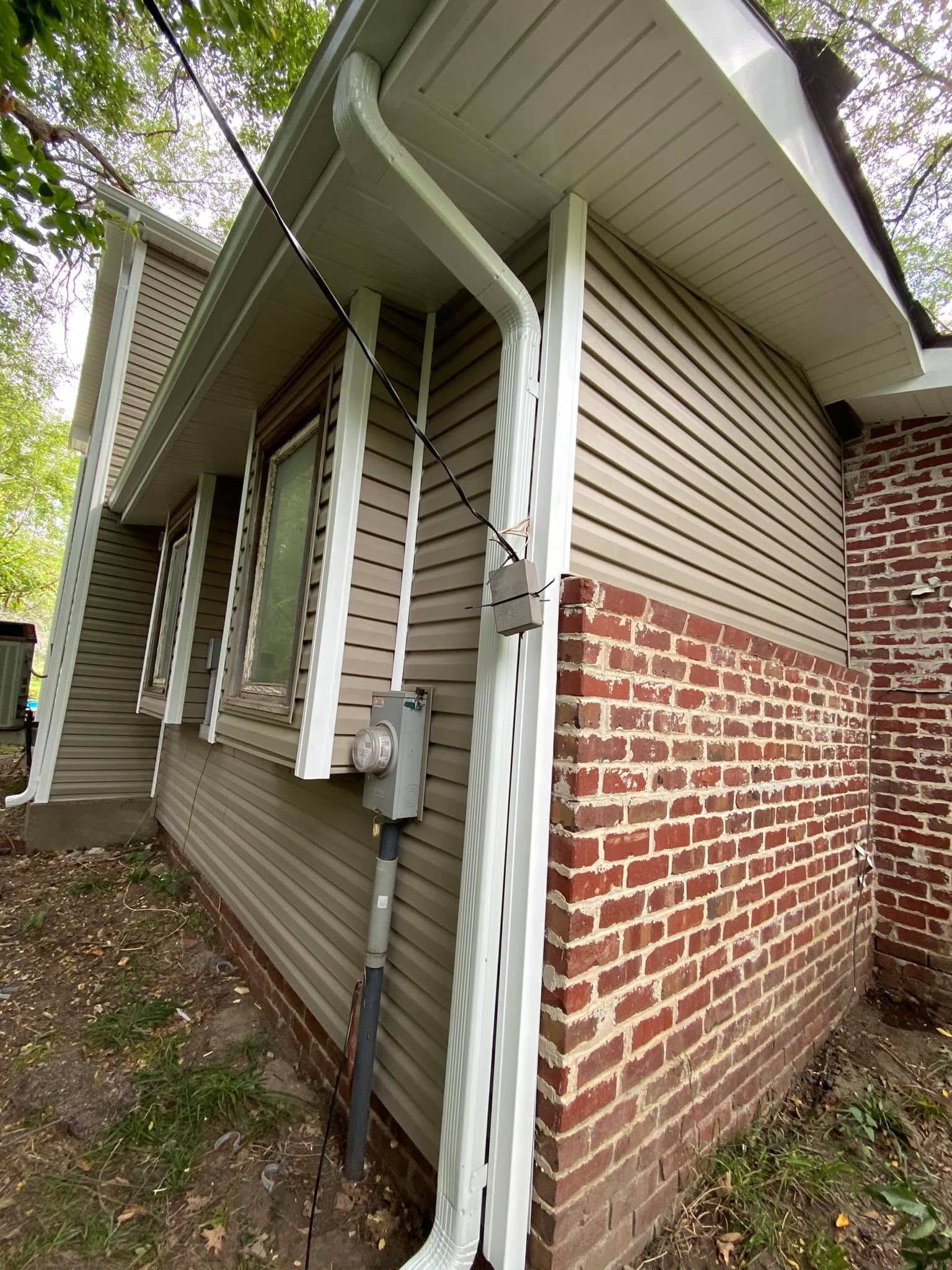 Side view of a brick-and-vinyl house with utility meter and downspouts under the eaves.
