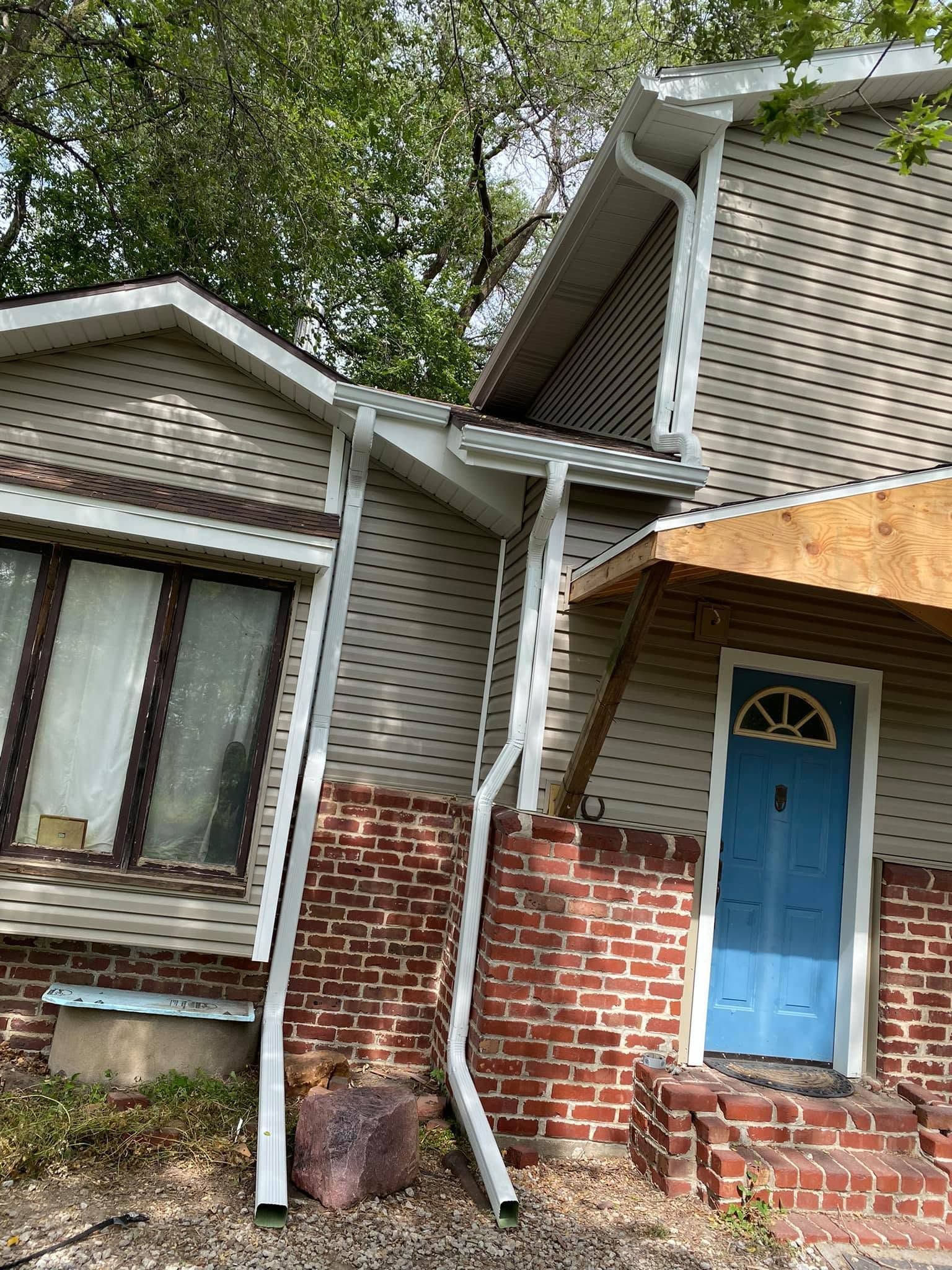 Damaged house exterior with bent gutter, cracked brick wall, and blue front door under a porch roof