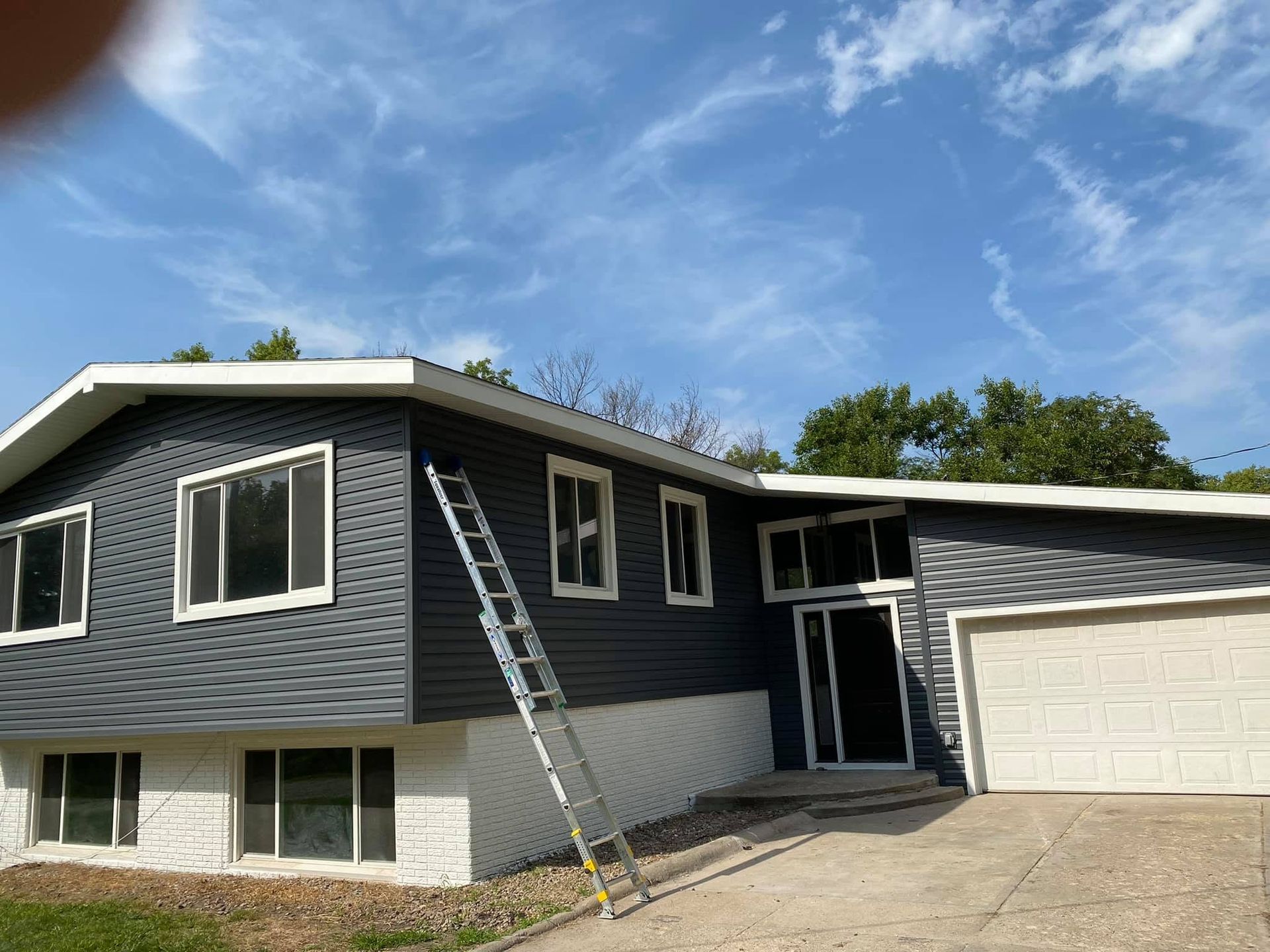 Two-story house exterior with ladder on the roof and attached garage under a blue sky
