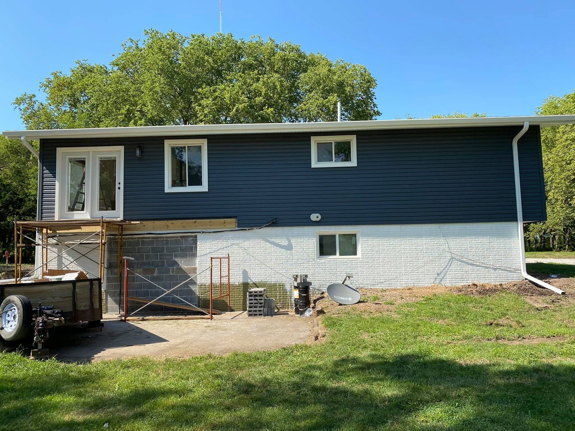 House exterior with dark blue siding, white foundation, and scaffolding under a partly finished front porch