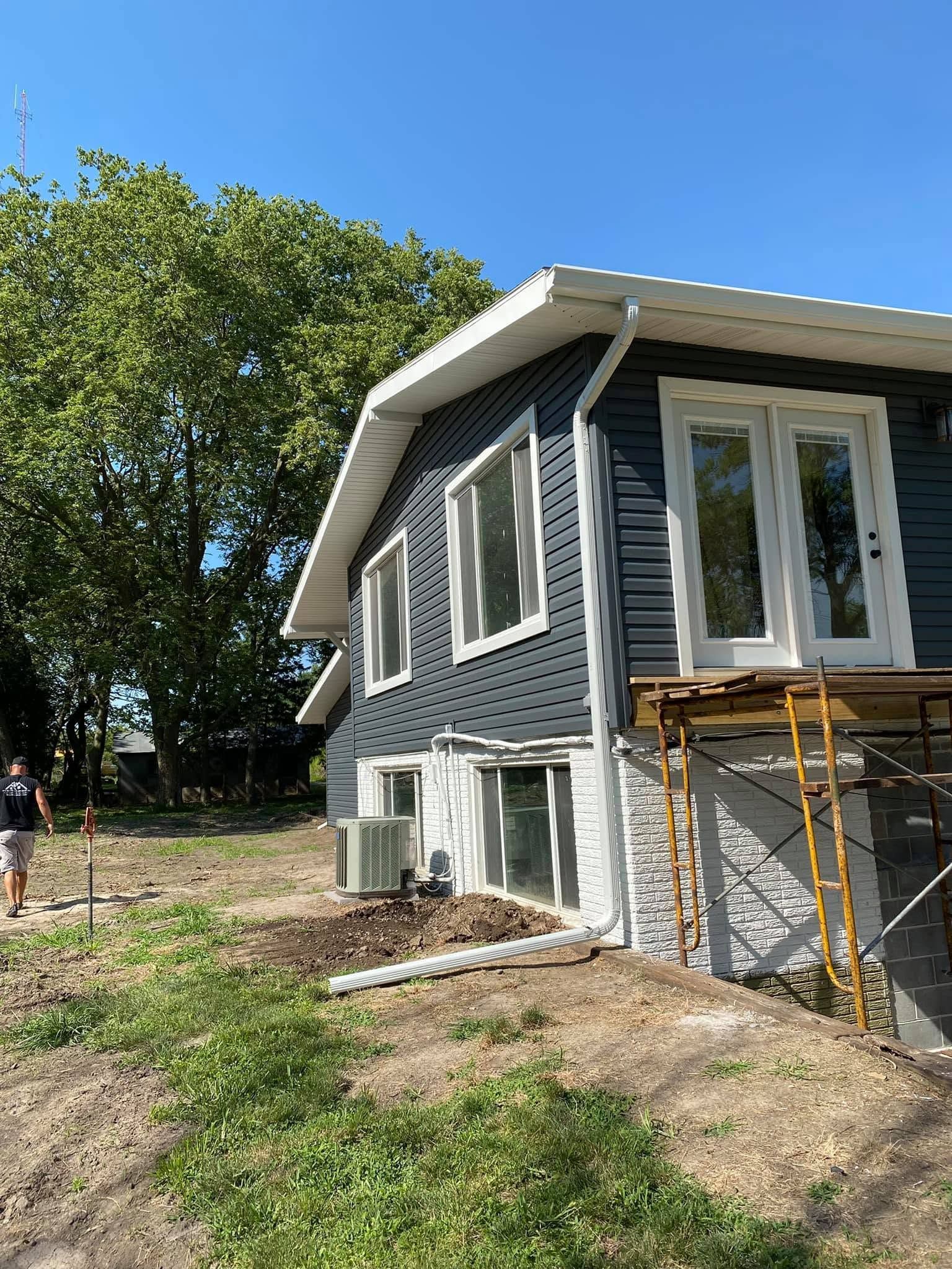 House under construction with blue siding, white windows, and scaffolding beside a grassy yard