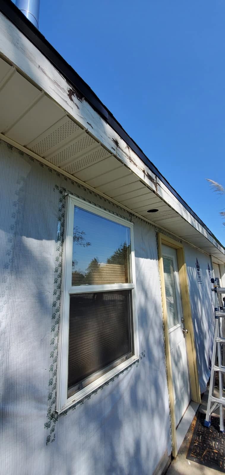 Side of a white house with a window, eaves, and blue sky above