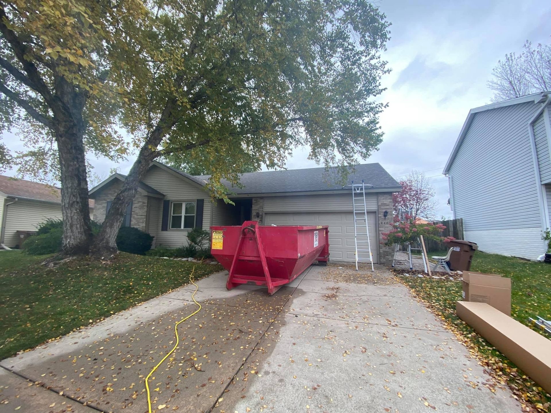 Residential driveway with a red dumpster in front of a house and trees overhead