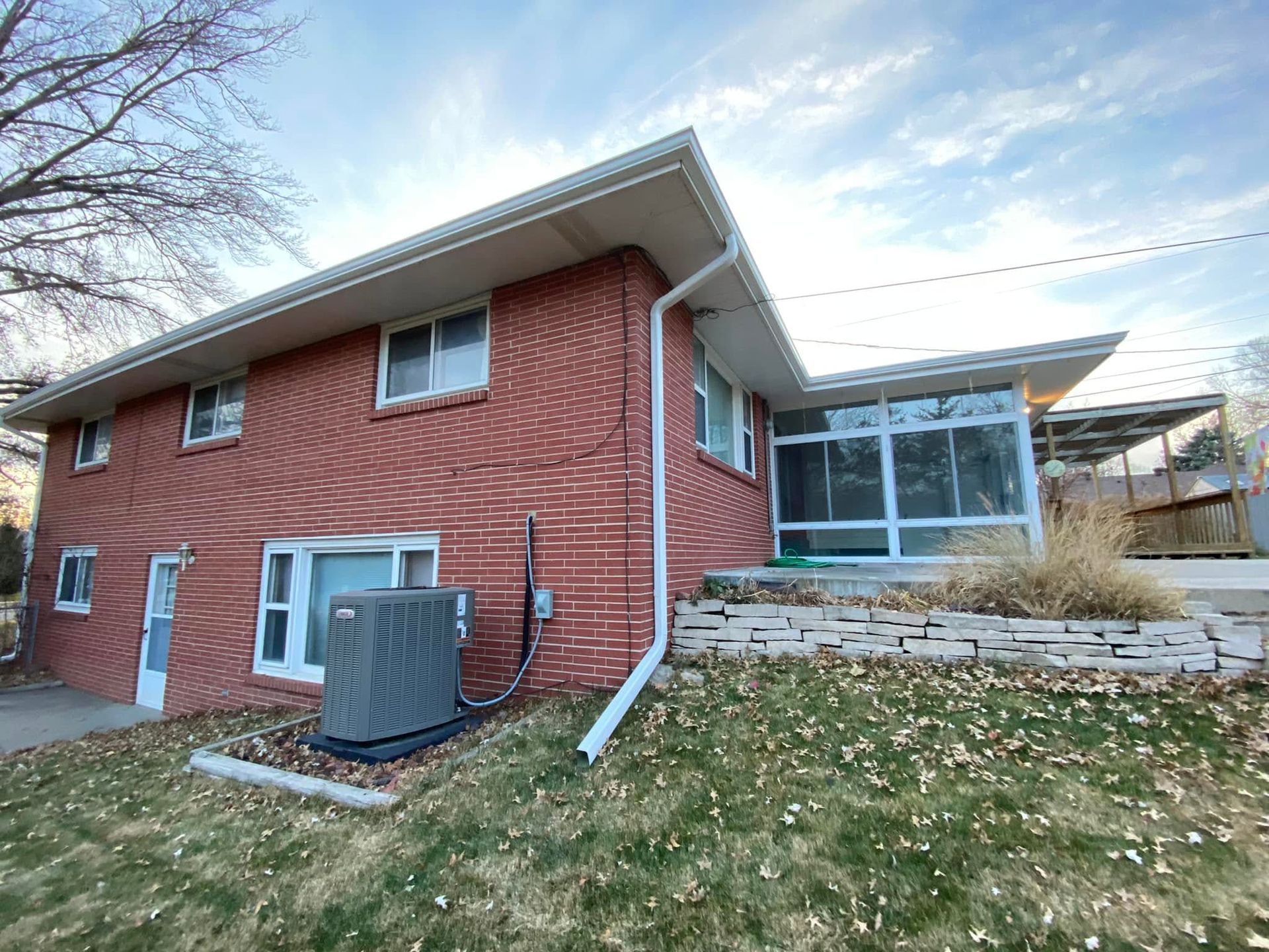 Red brick house exterior with white trim, a small porch, and an HVAC unit beside the wall.