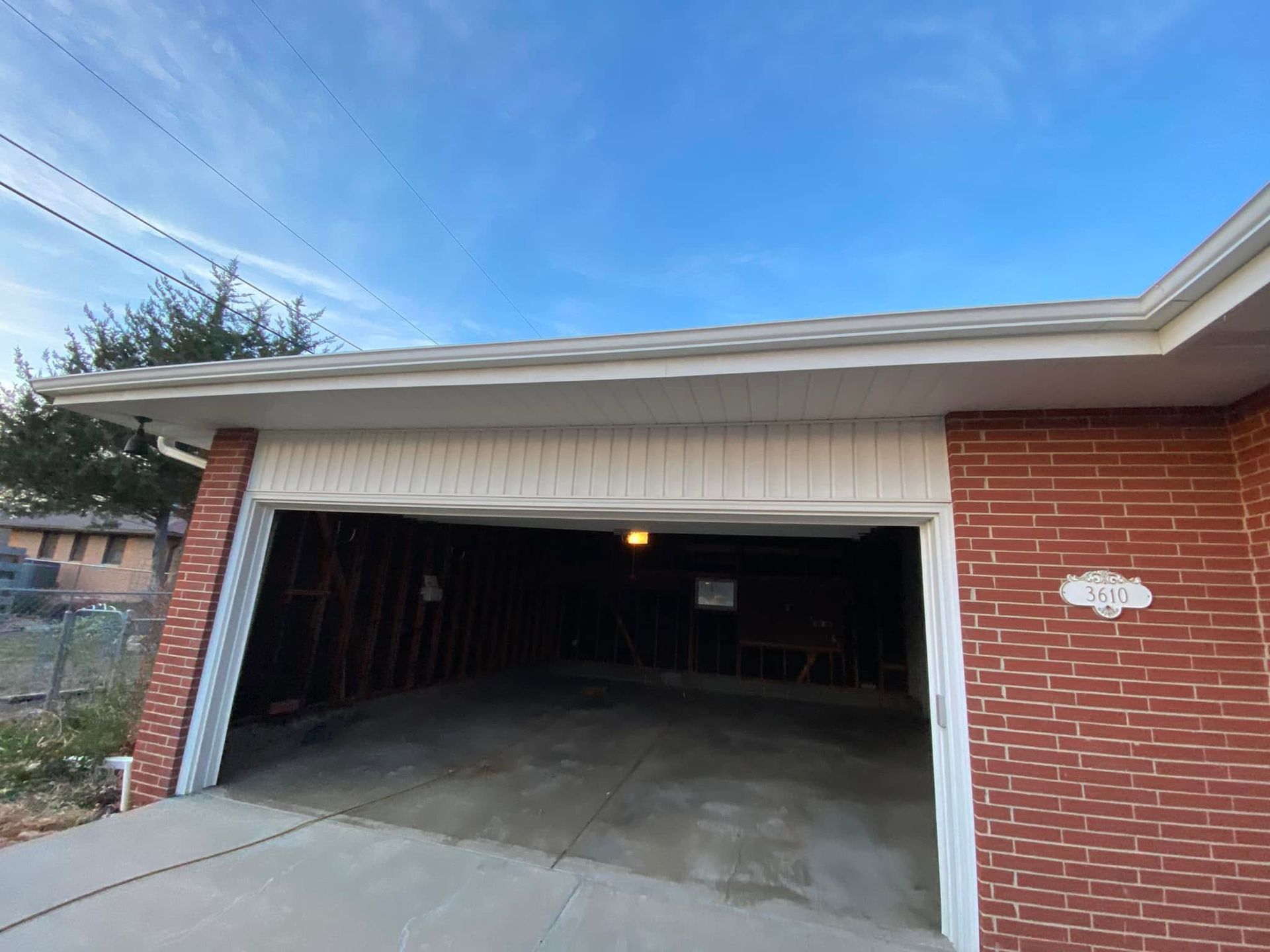 Open garage with concrete driveway, brick exterior, and a lit ceiling light inside.