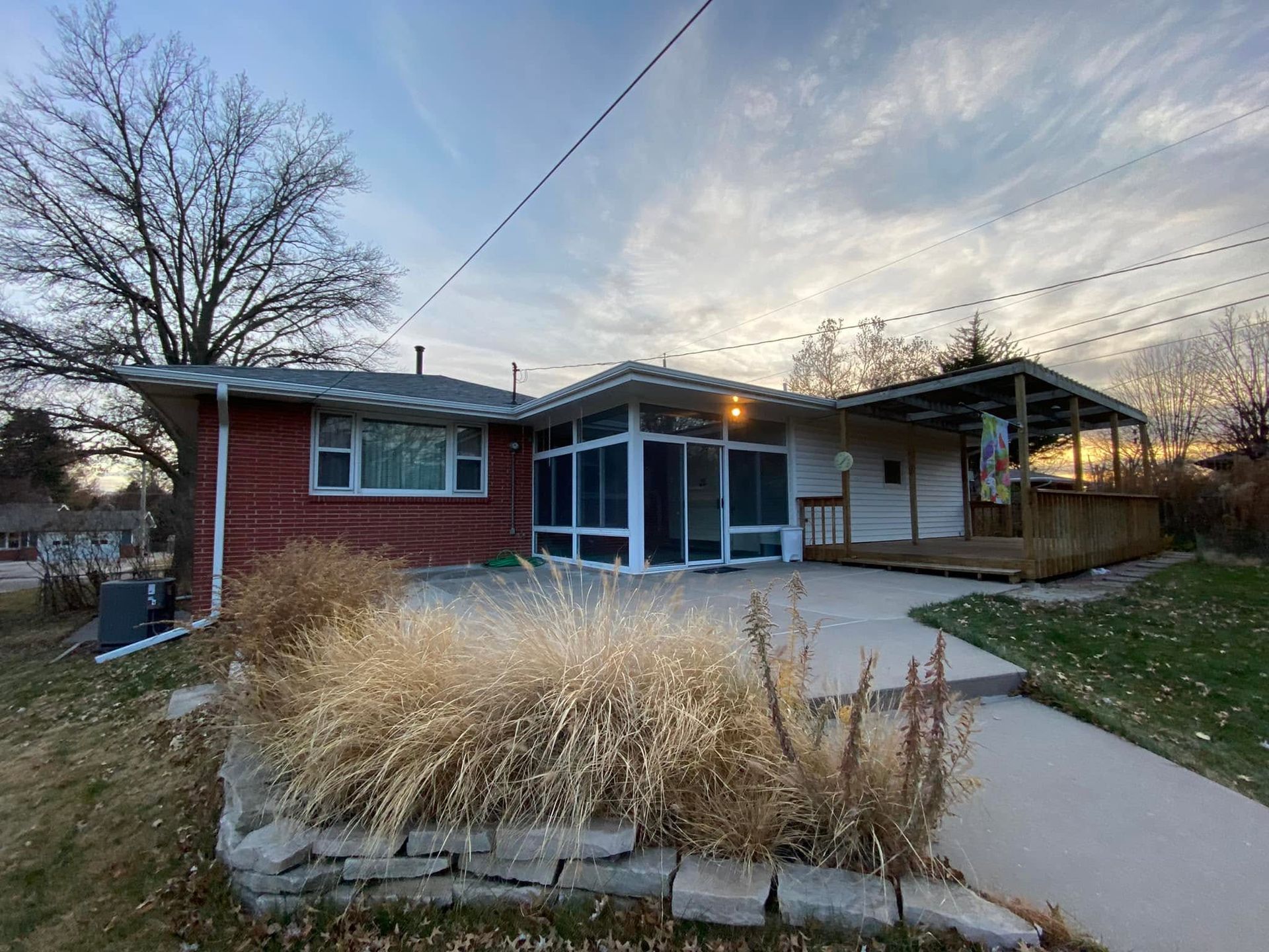 Small red house with a covered porch, concrete walkway, and tall ornamental grass at dusk.