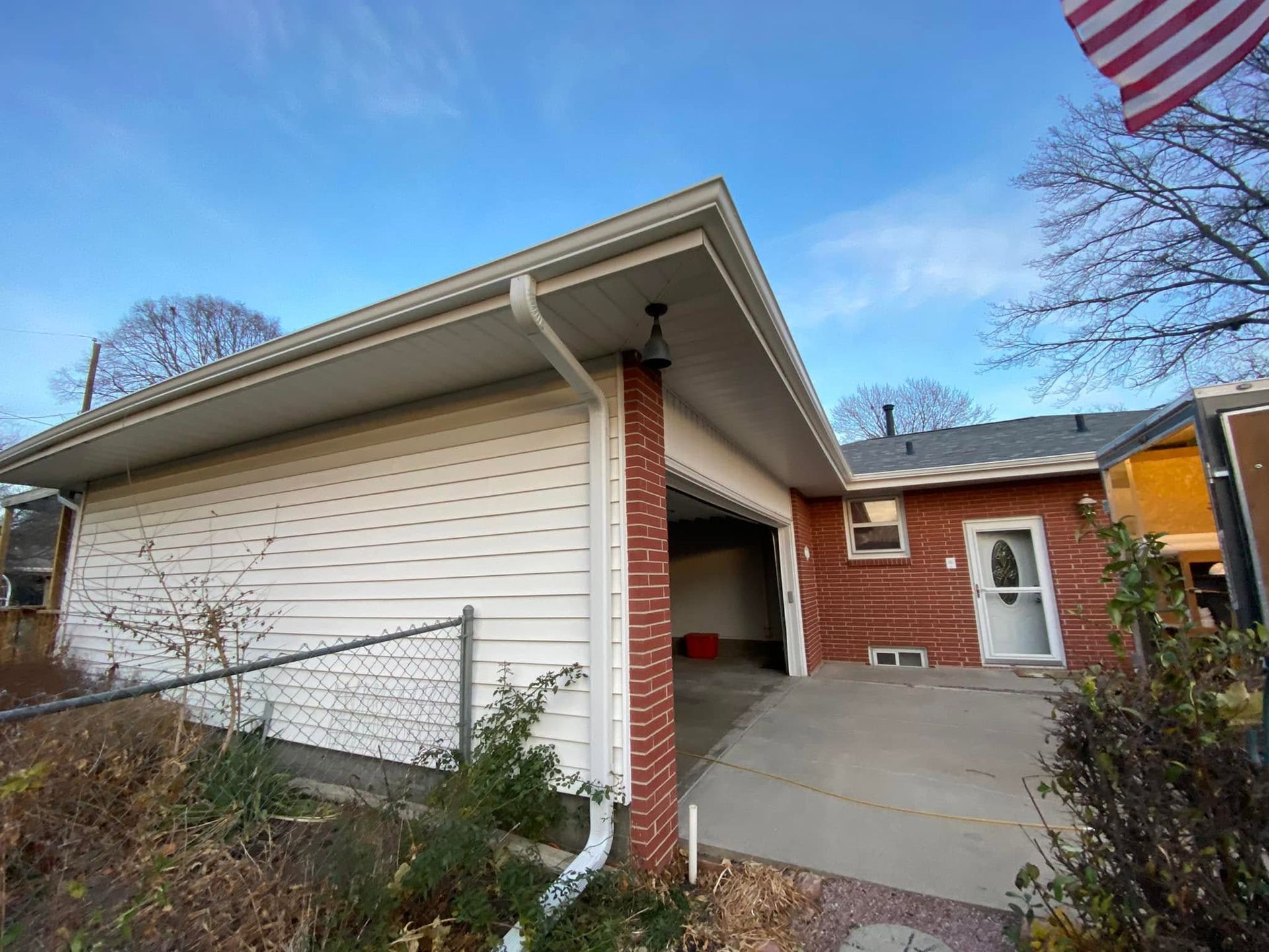 Suburban house exterior with white siding, red brick, driveway, and an American flag overhead
