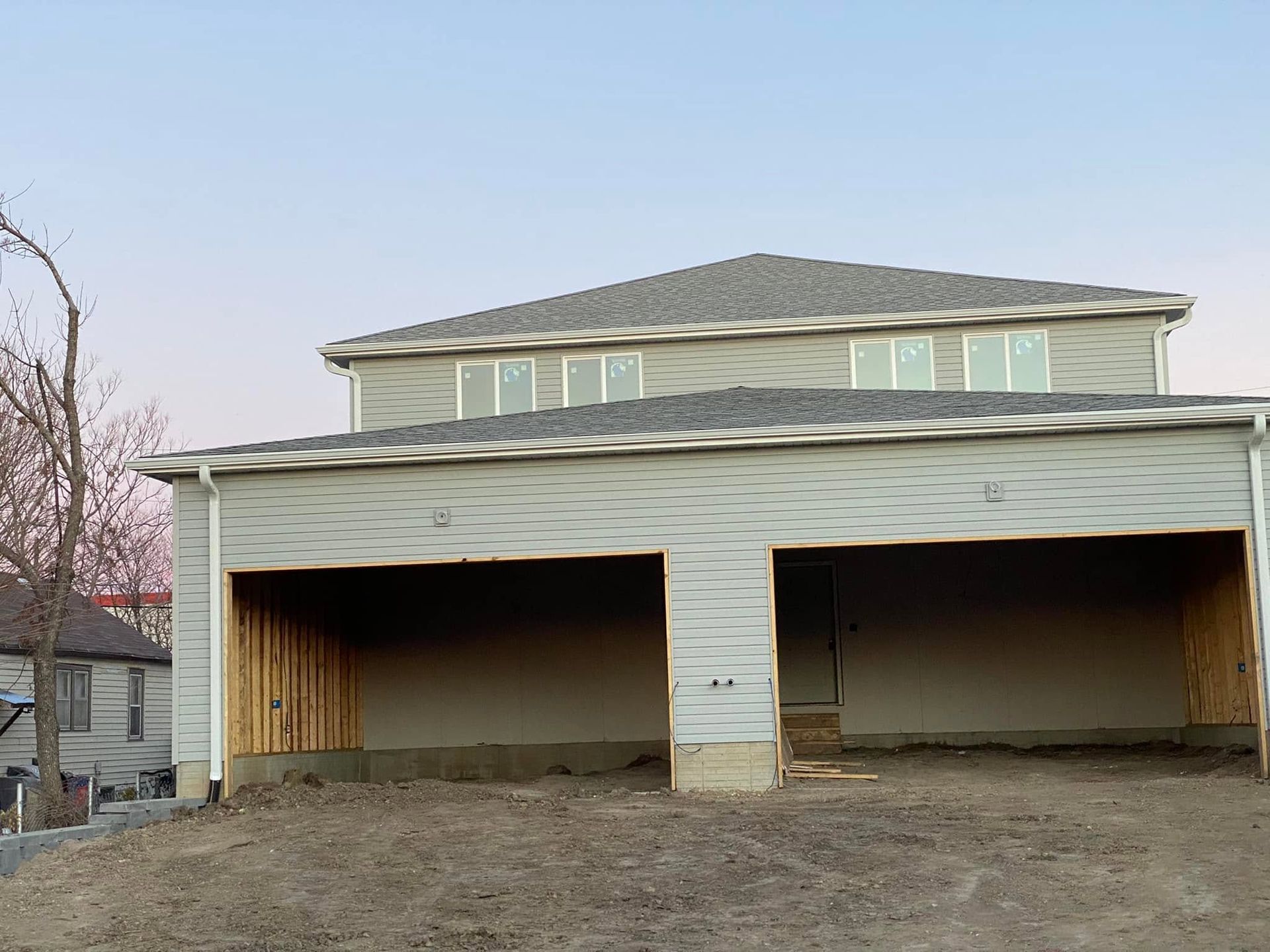 Two-story house under construction with a wide unfinished garage and dirt foreground.