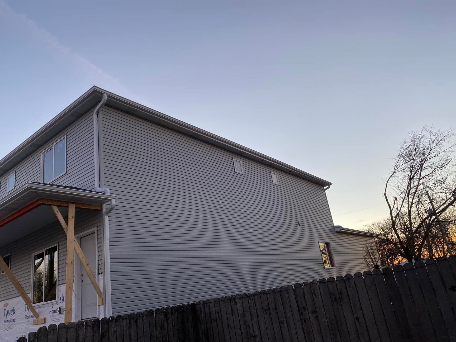 Two-story white house with a wavy patterned exterior beside a dark fence at sunset