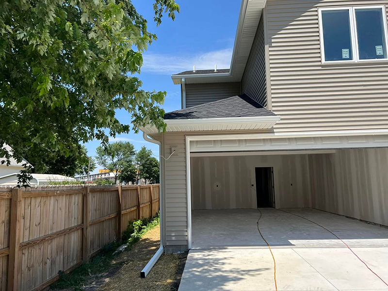 Backyard view of a beige house with open garage, wooden fence, and tree at left