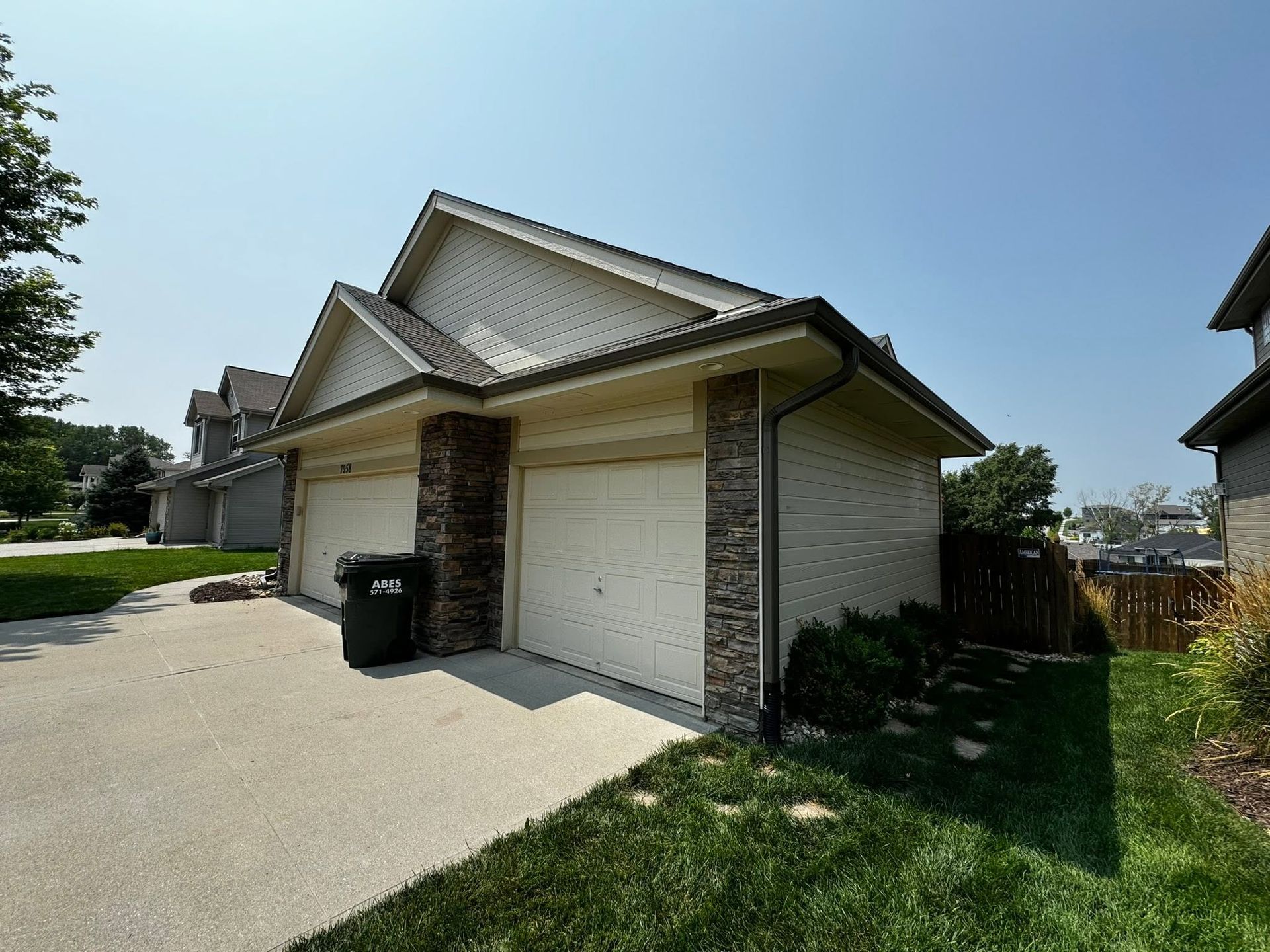 Suburban house exterior with double garage, driveway, and trash bin on a sunny day