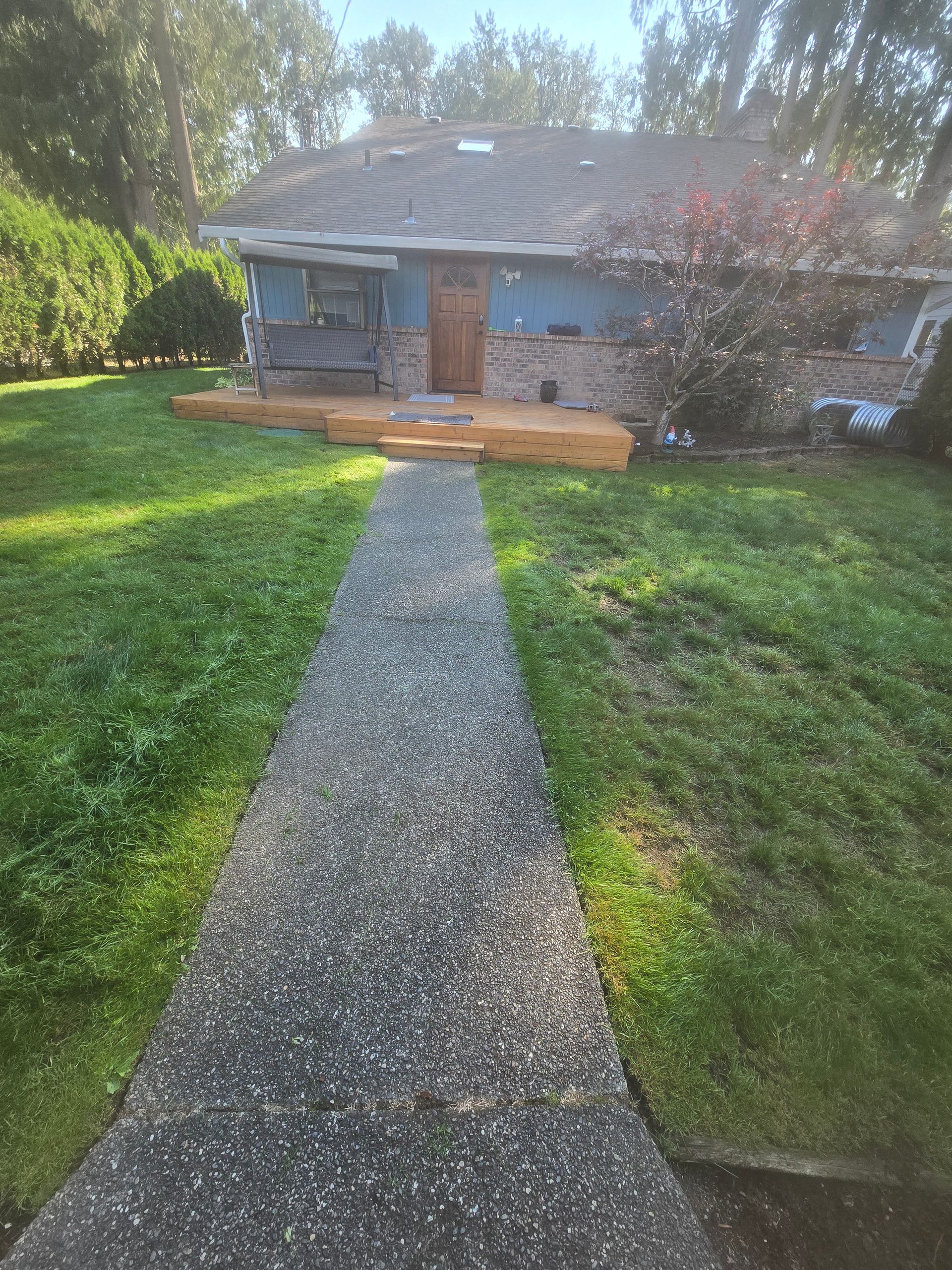 Stone walkway leading to a small gray house with a brick porch in a sunny yard.
