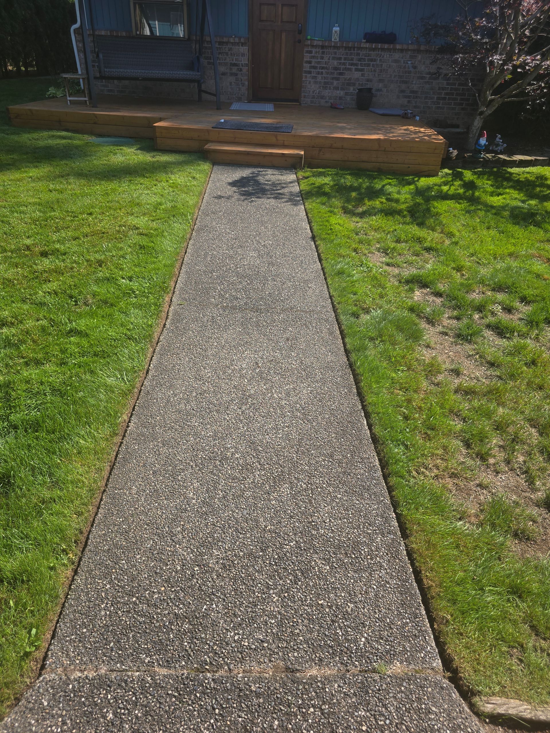 Concrete walkway through green lawn leading to a house with a small wooden step at the entrance.