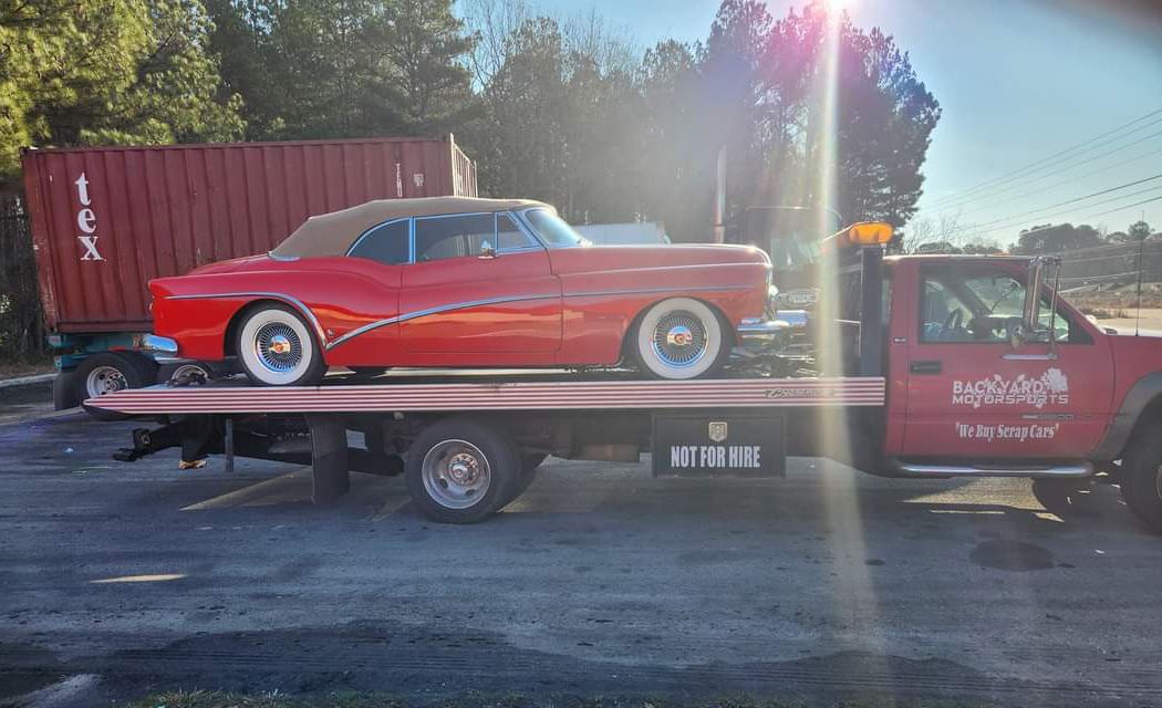 A red car is being towed by a tow truck.