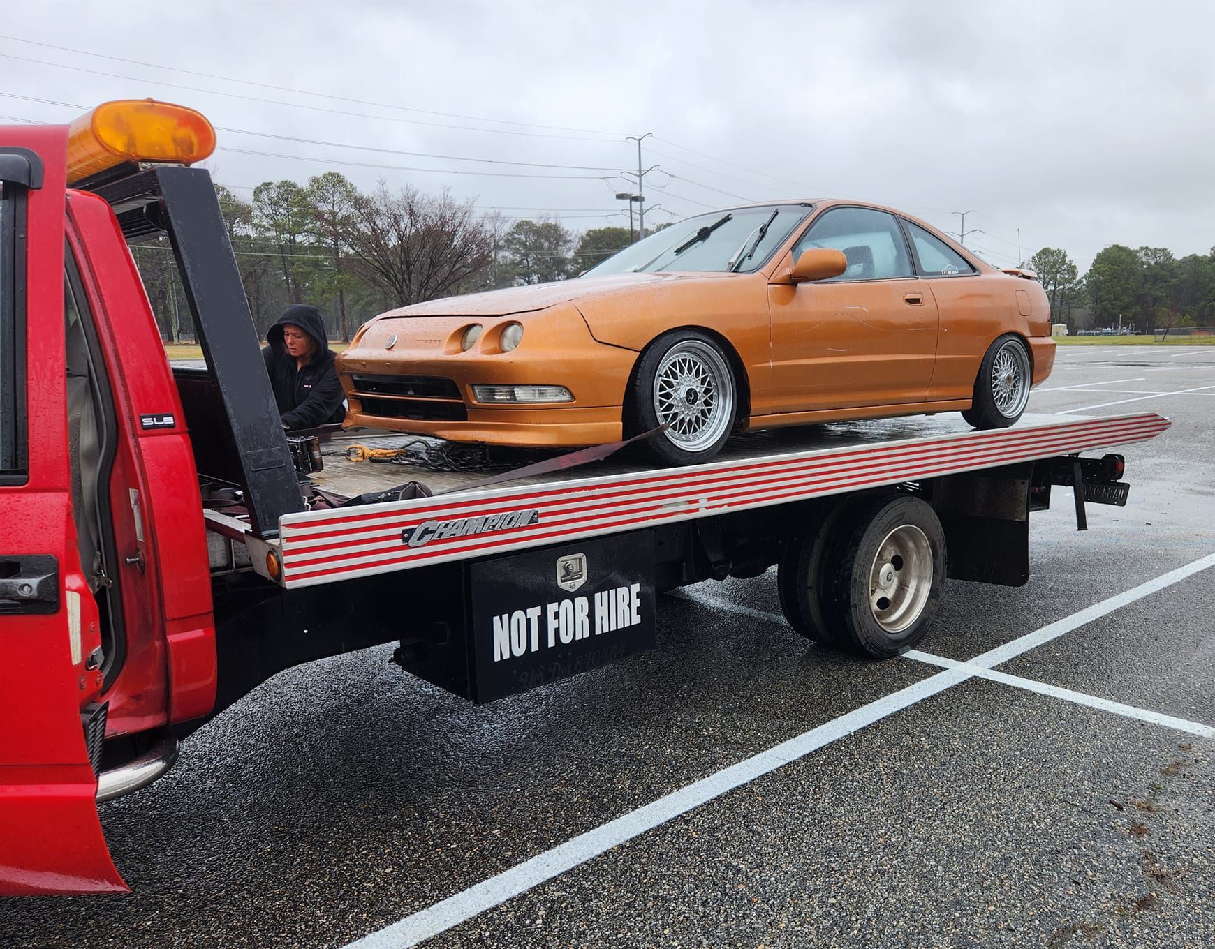 A tow truck is towing a car in a parking lot.