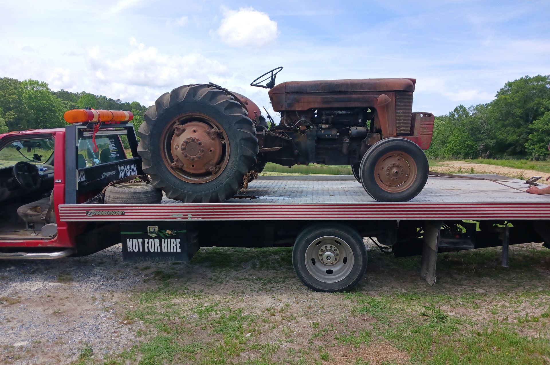 An old rusty tractor is sitting on top of a flatbed tow truck.