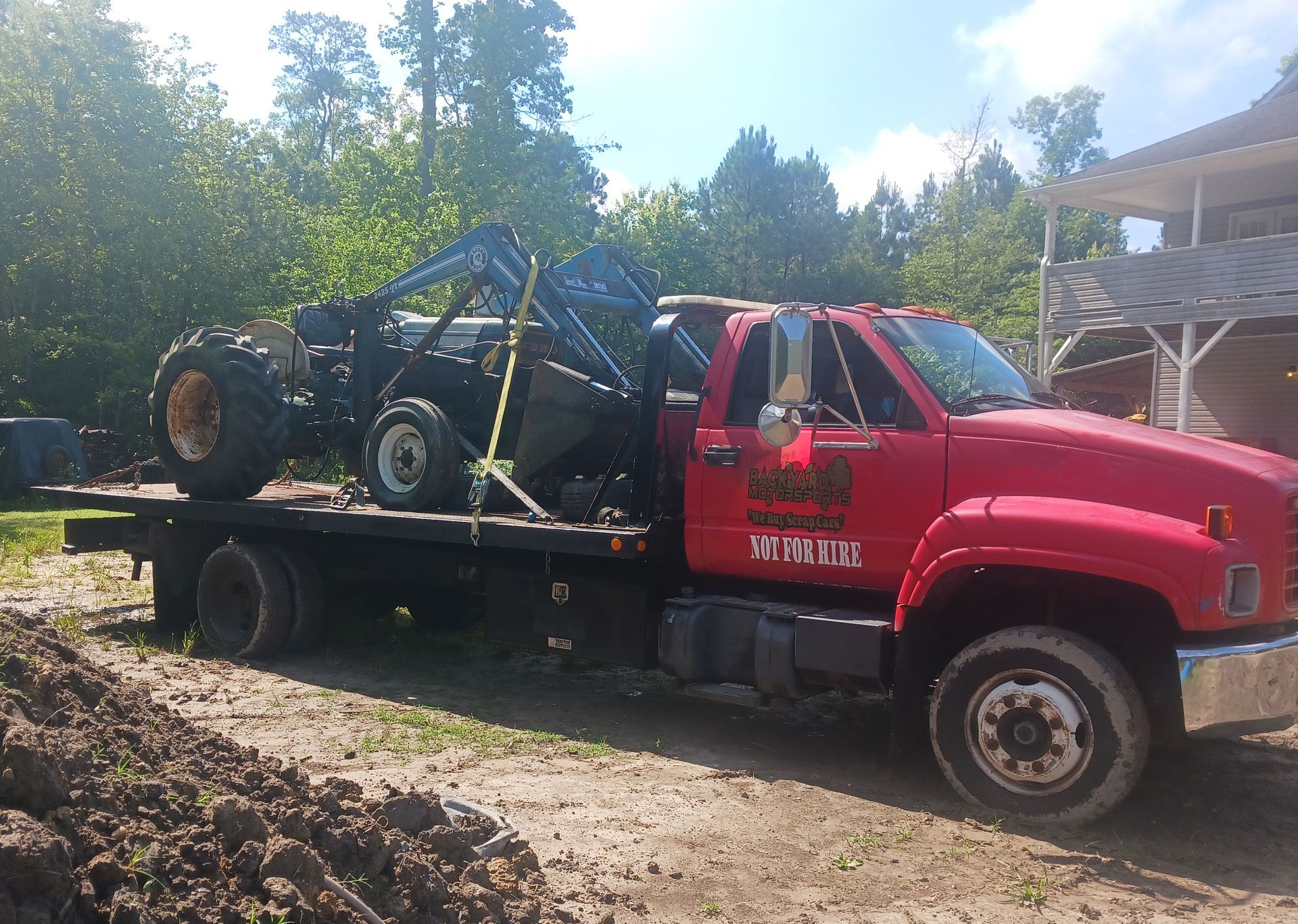 A red tow truck is carrying a tractor on the back