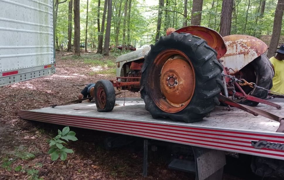 An old tractor is sitting on the back of a tow truck.
