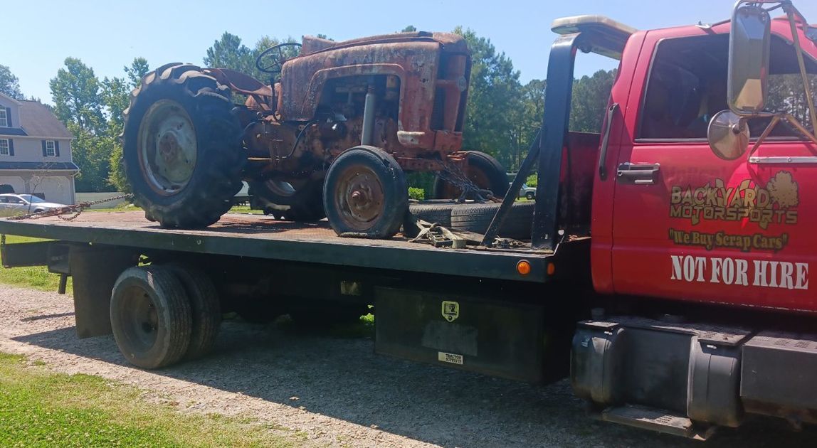 An old rusty tractor is being towed by a tow truck.