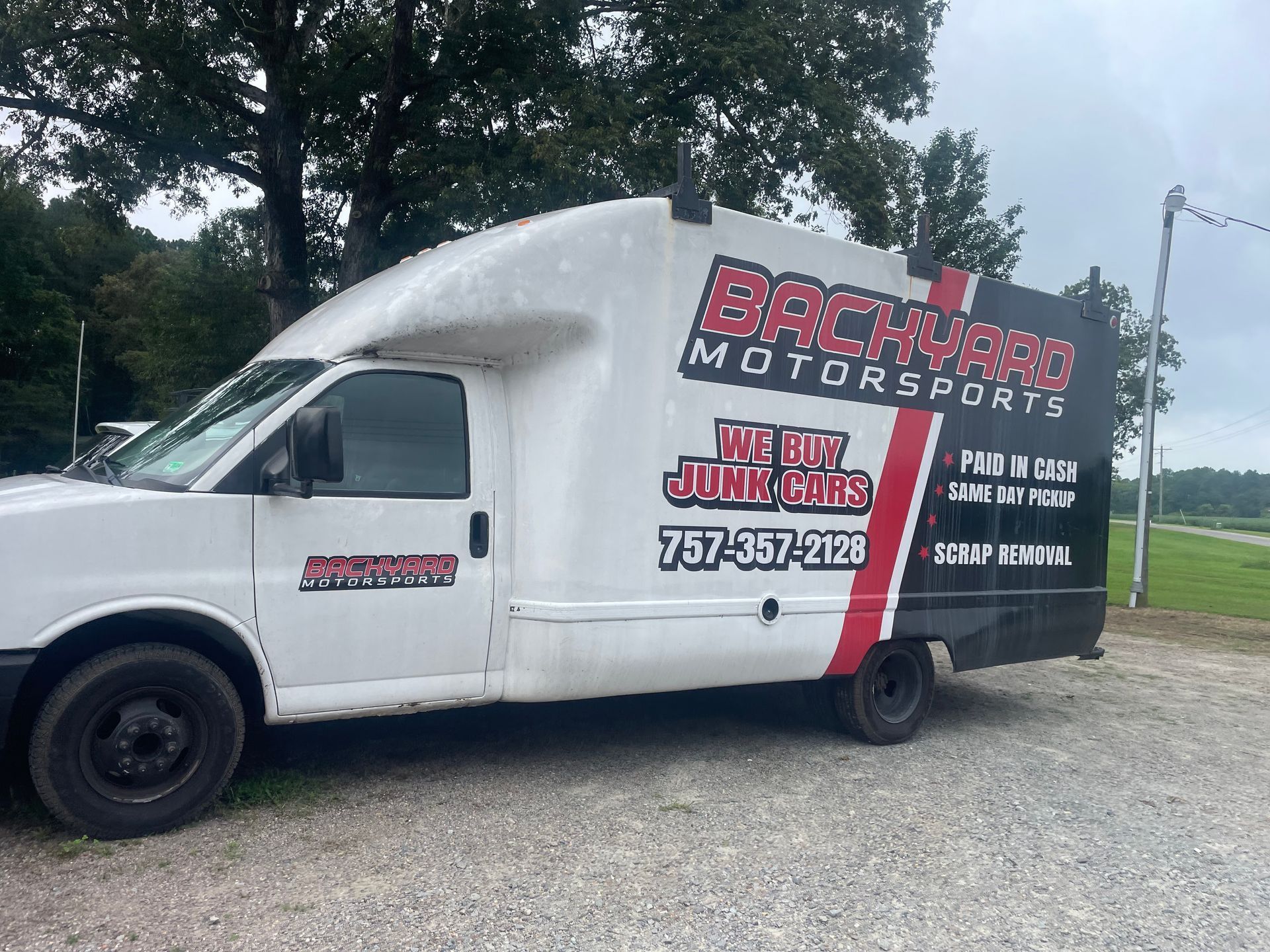 A backyard motorsports van is parked in a gravel lot