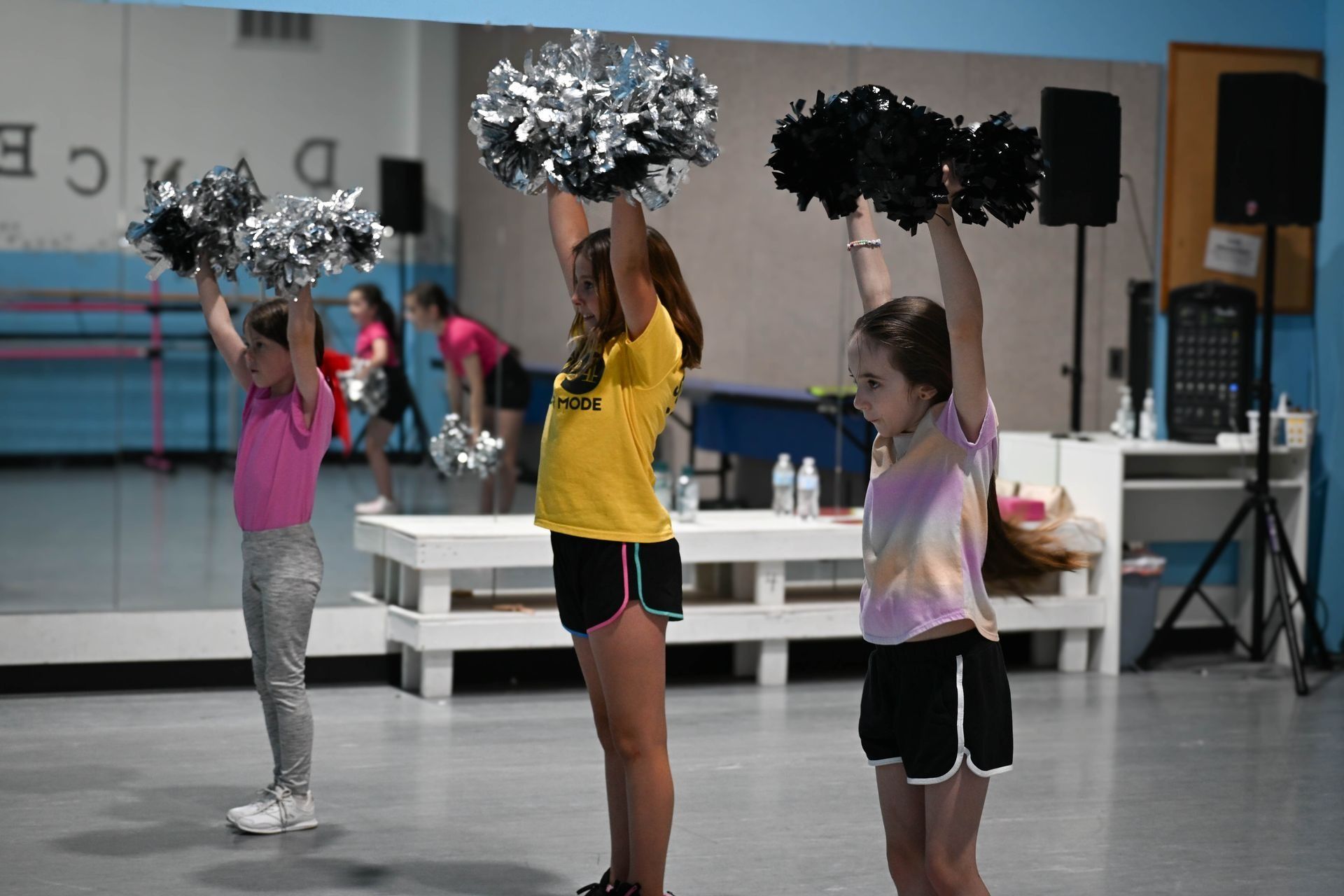 Three children in dance practice holding pom-poms in a studio.