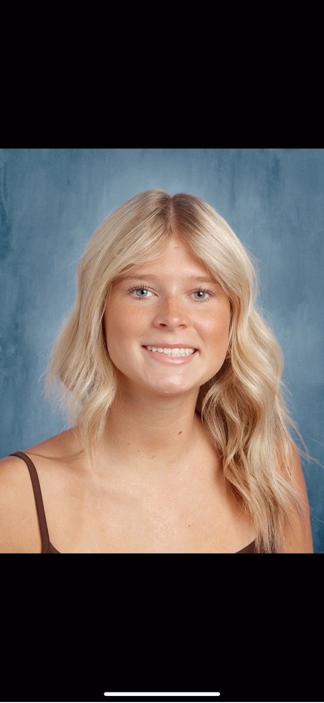 Smiling blonde person in a black top against a blue studio backdrop