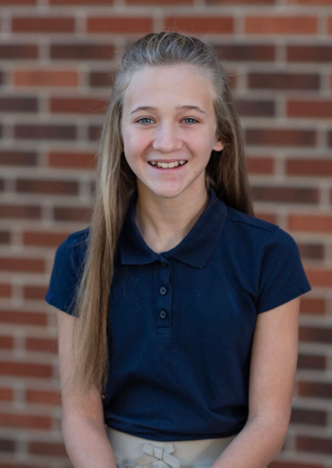 Smiling person in a navy polo shirt standing before a brick wall