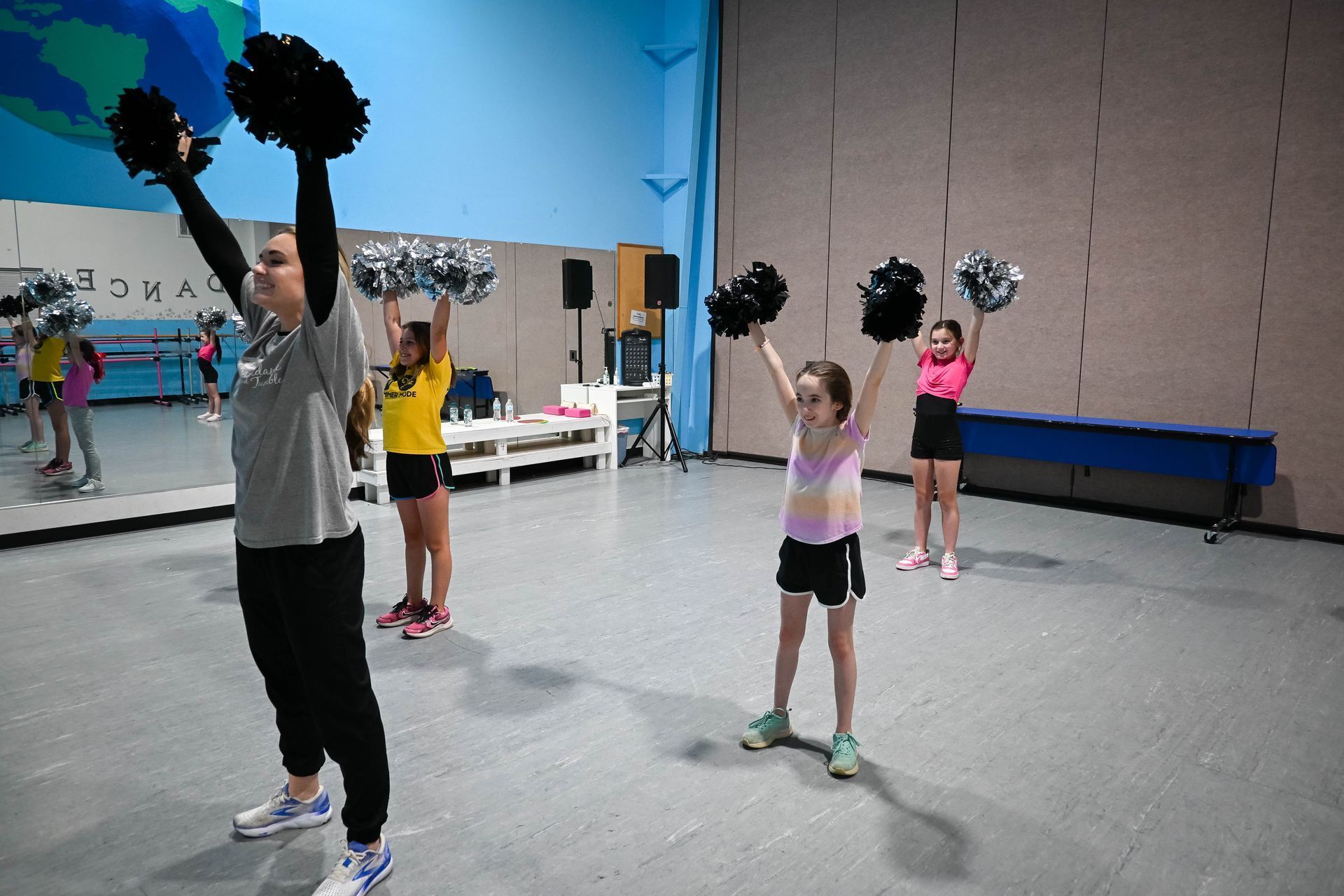 Group exercise class in a gym, with people raising black and silver pom-poms overhead.