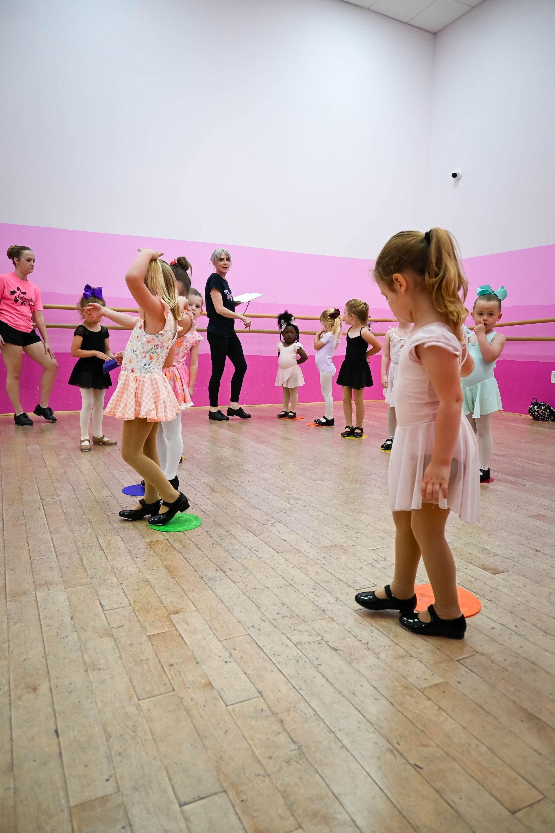 Children practicing dance in a studio with pink walls and a wooden floor.